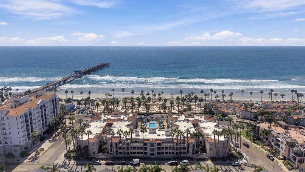 Aerial view of Oceanside beachfront condominiums, palm-lined beach, pier, and Pacific Ocean.