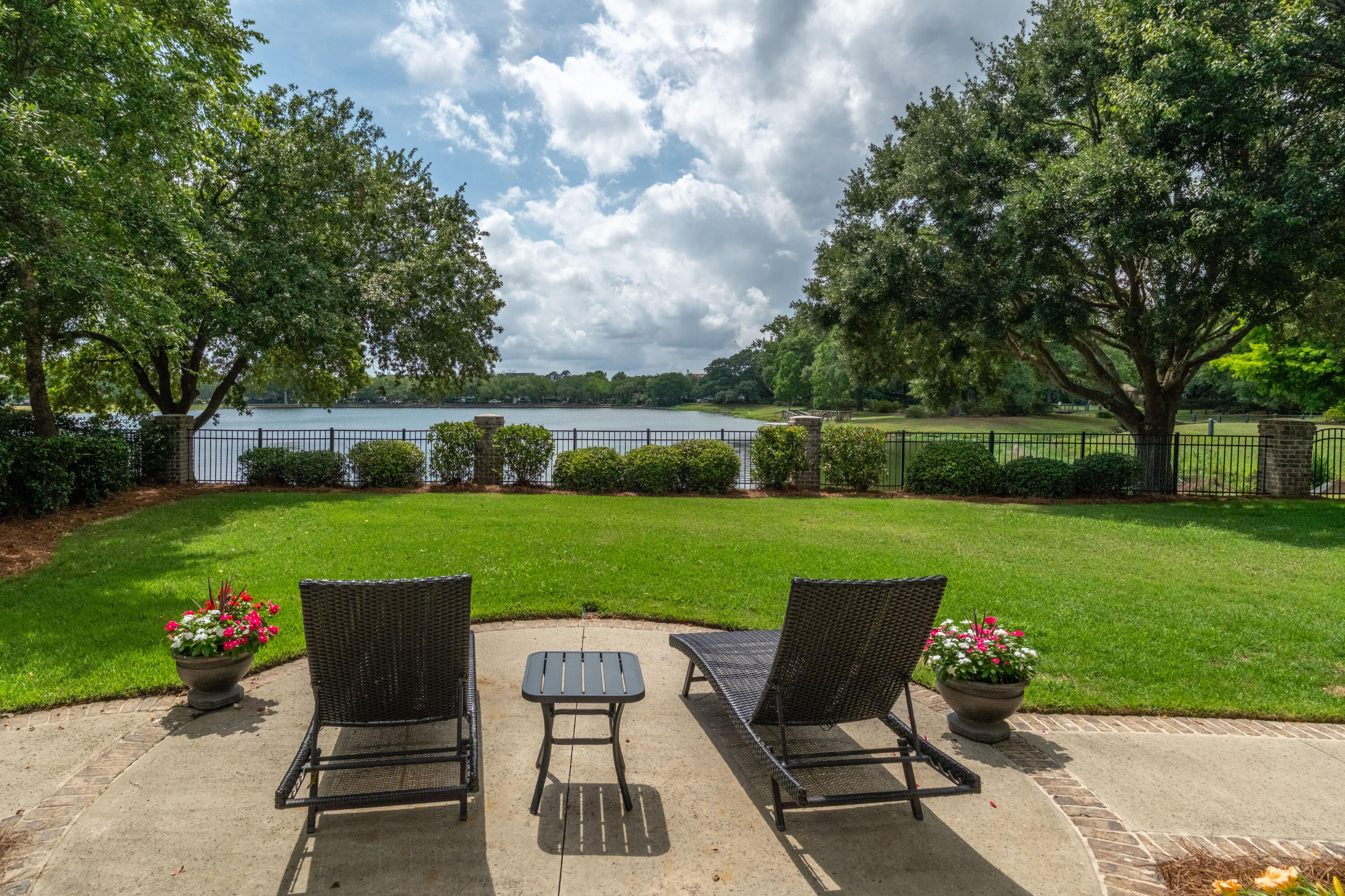 Furnished patio overlooking a lake, with wicker lounge chairs, a lawn, and mature trees.