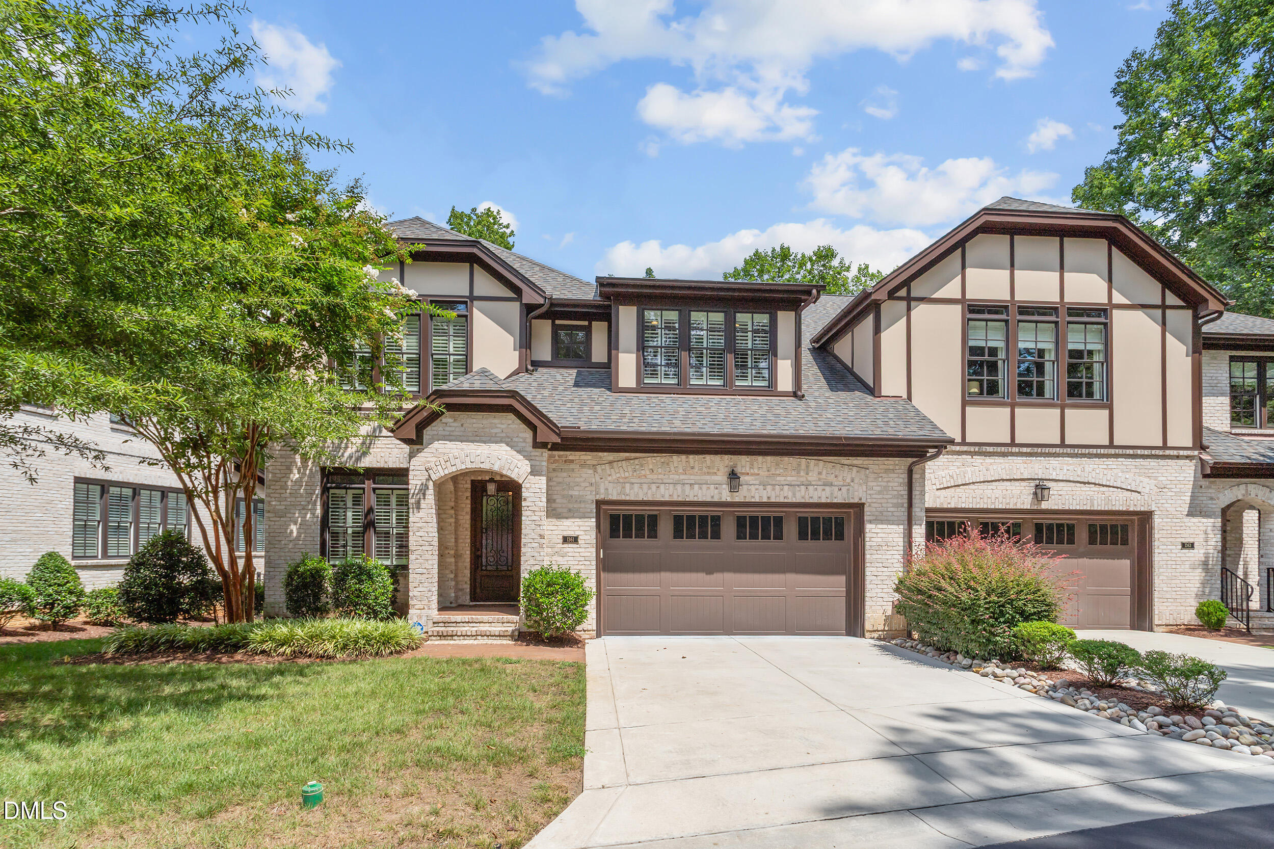 Two-story half-timbered home with a brick façade, two-car garage, broad driveway, and landscaped front yard.