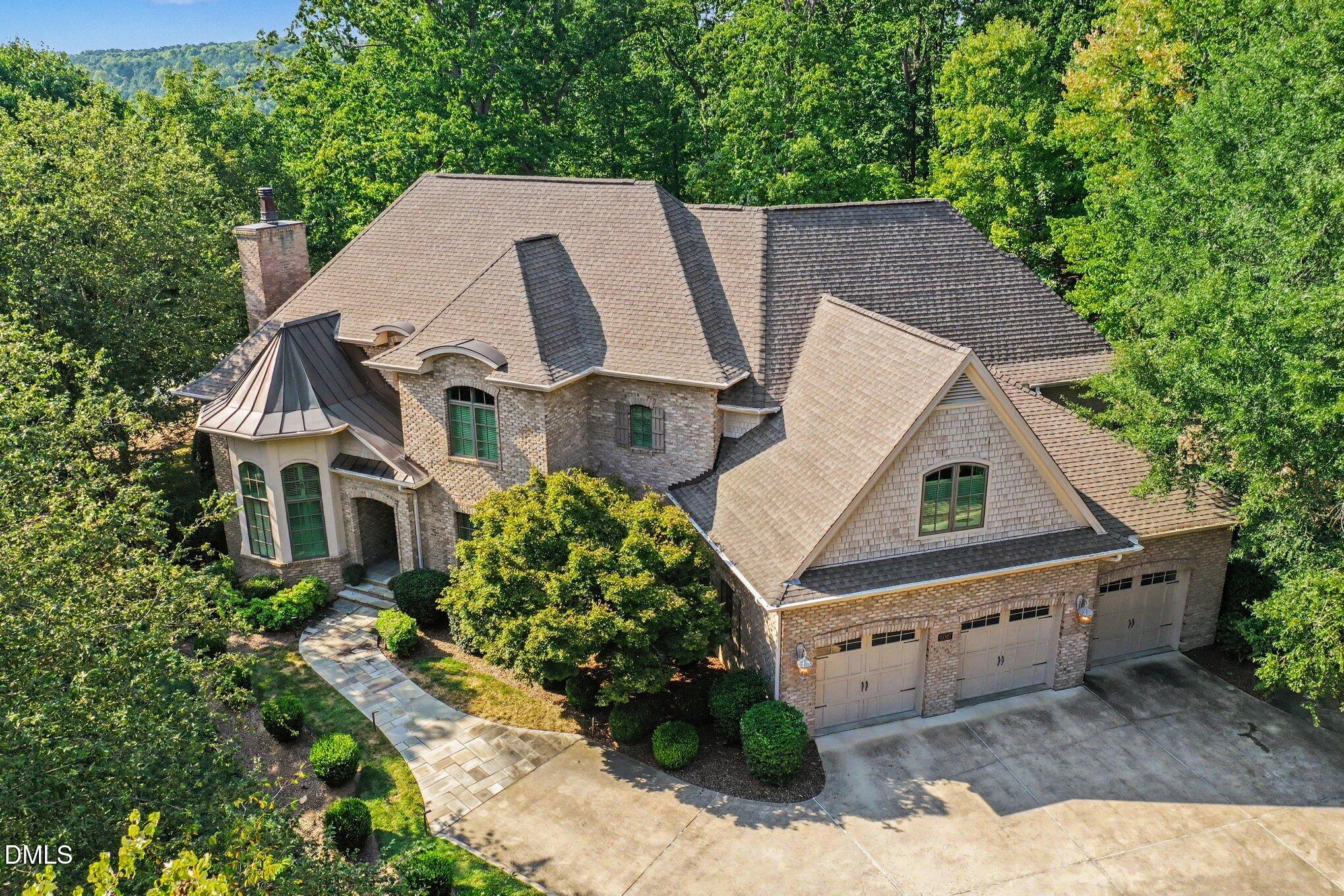 Aerial view of a brick home with a turret, landscaped grounds, and a three-car garage.
