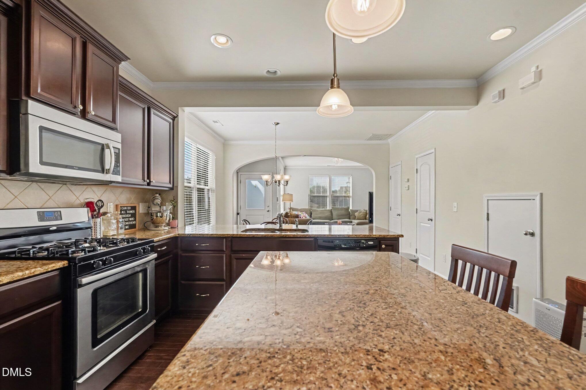 Kitchen with dark wood cabinets, stainless steel appliances, and a granite peninsula overlooking the living room.