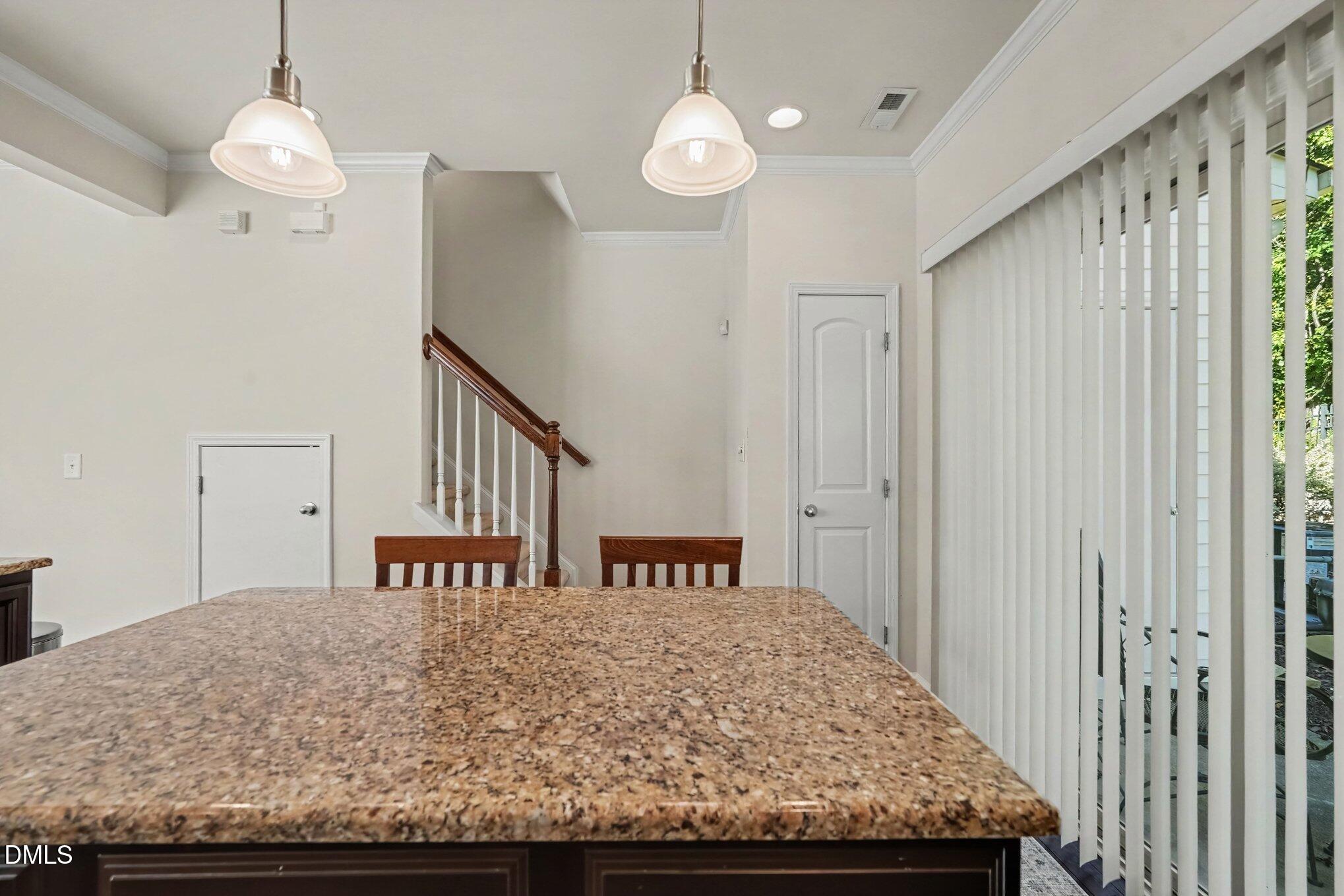 Kitchen with a large speckled granite island, pendant lights, and sliding glass door with vertical blinds.