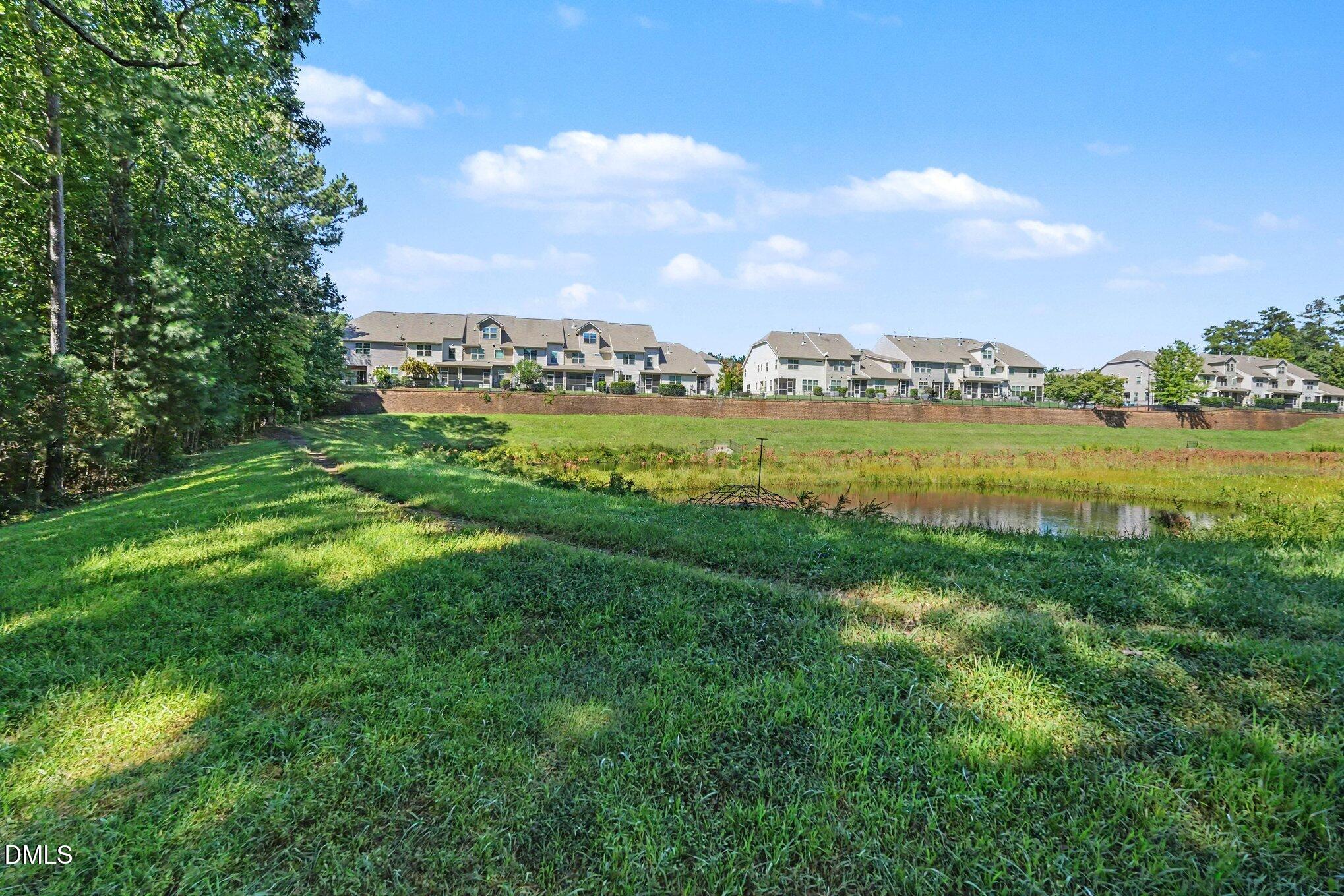 Pond and grassy bank with attached homes across the water and mature trees to the left.
