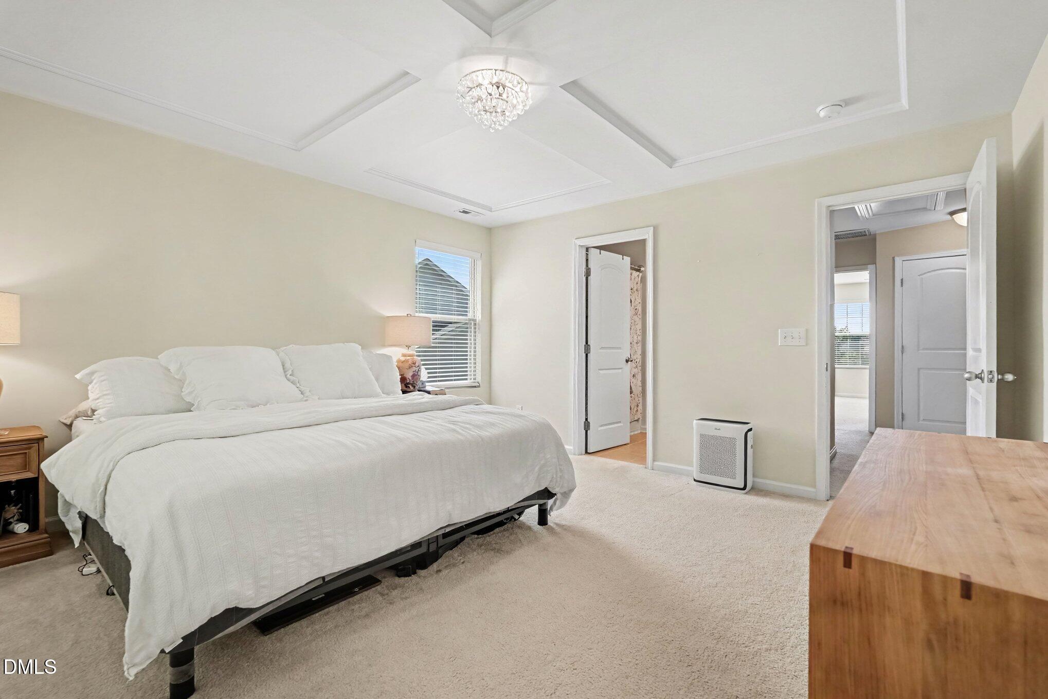 Bedroom with white bedding, a tray ceiling, and a crystal chandelier.