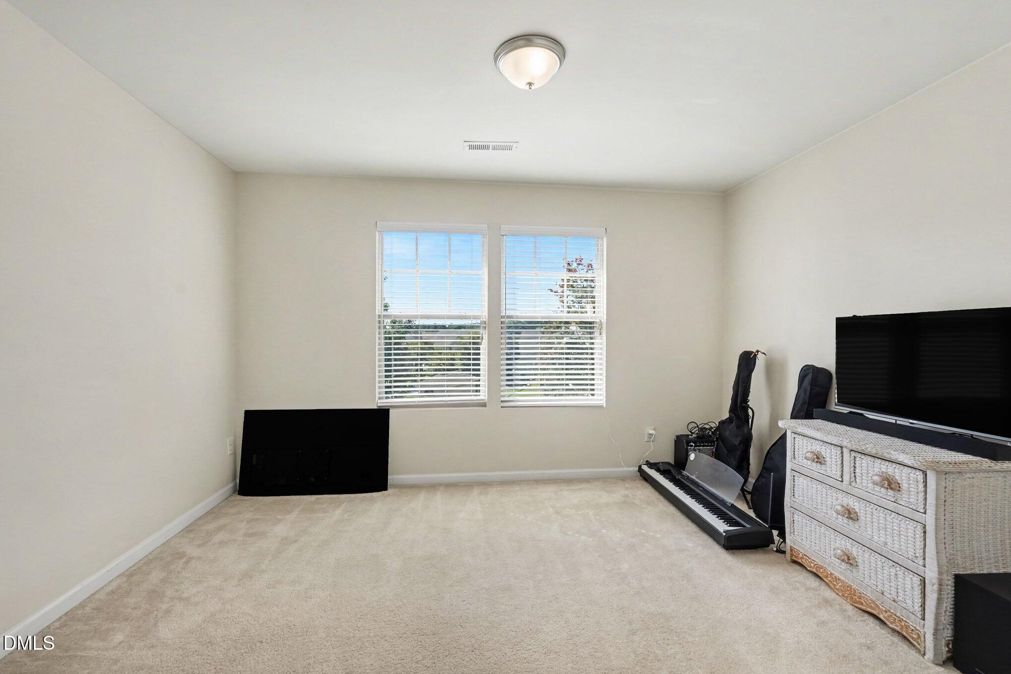 Carpeted bonus room with two windows, a television, and a digital piano.