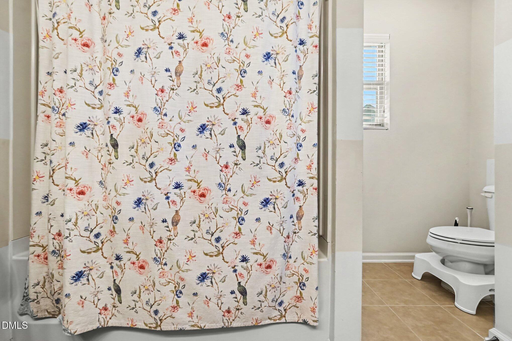 Bathroom with a bird-and-flower shower curtain, toilet, and small window.