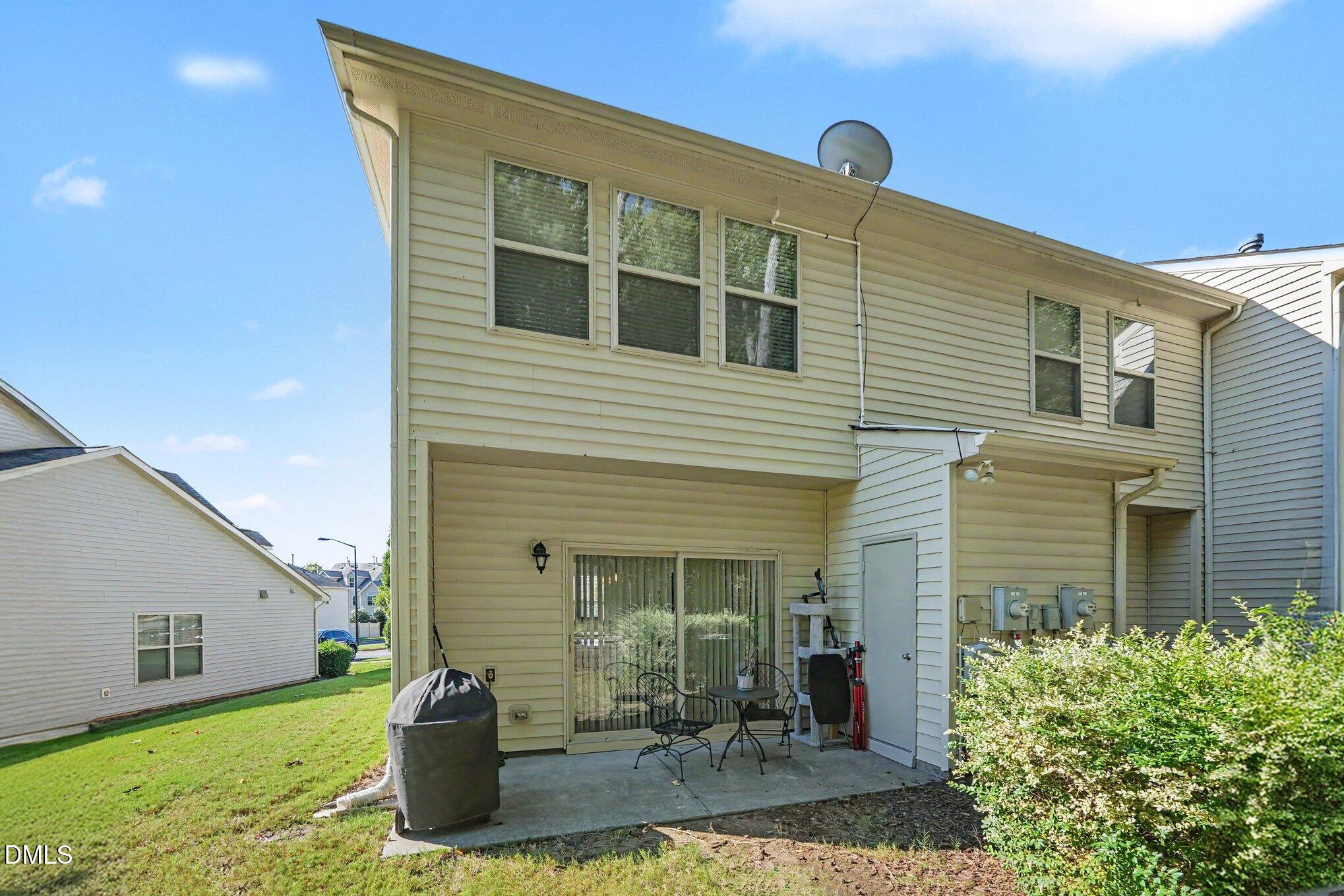 Rear of a two-story beige-sided home with a patio, sliding glass door, and lawn.