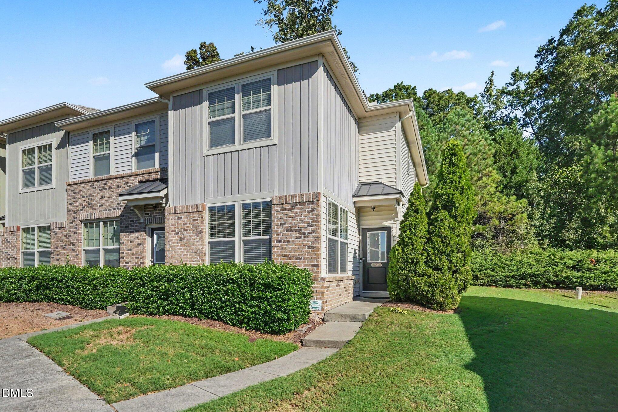 Two-story townhouse with gray siding, brick facade, and a landscaped front lawn.