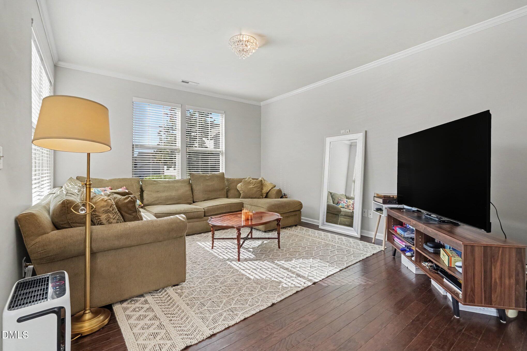 Living room with a tan sectional, patterned rug, large television, and dark hardwood floors.