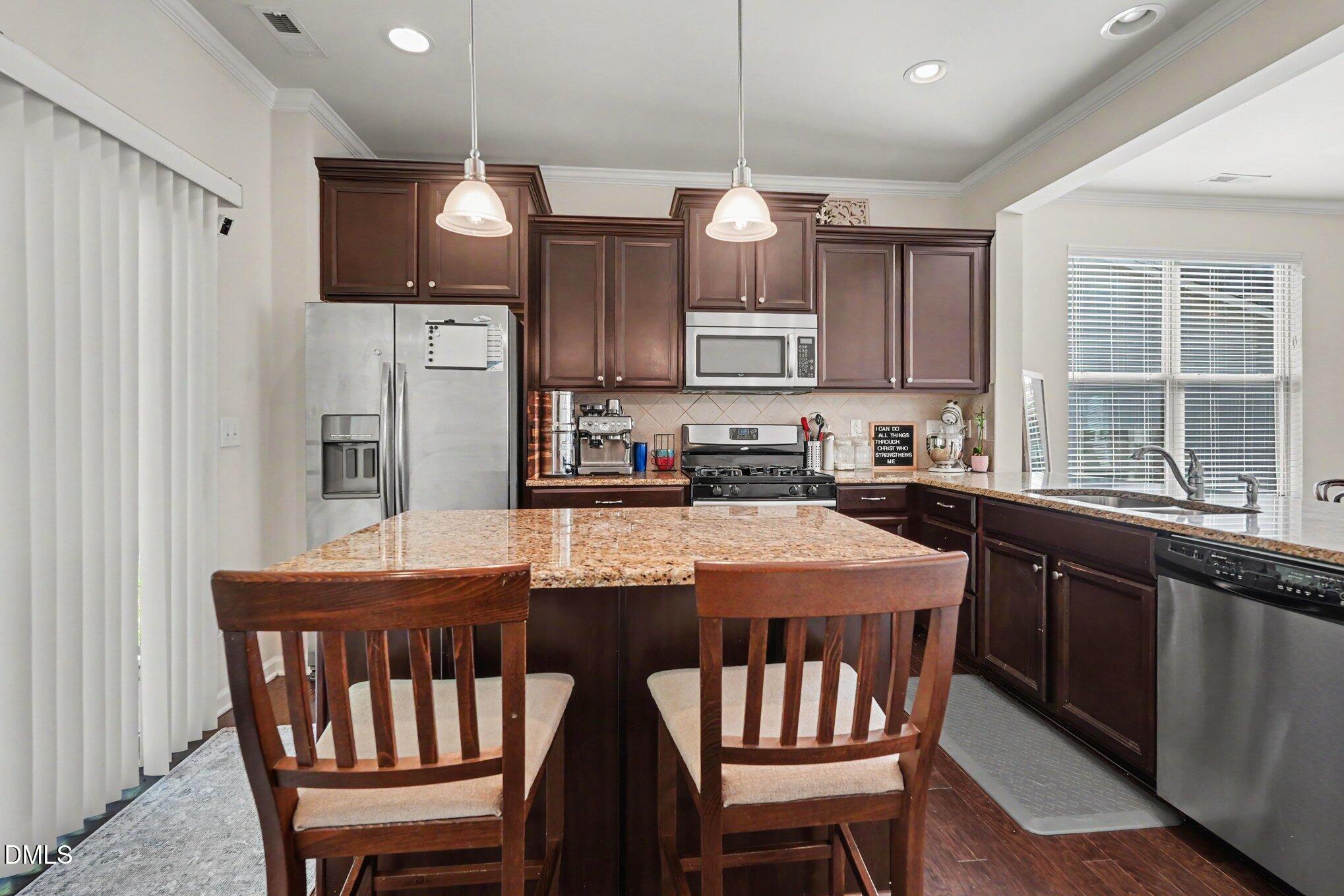 Kitchen with dark wood cabinets, stainless steel appliances, and a granite island with two chairs.