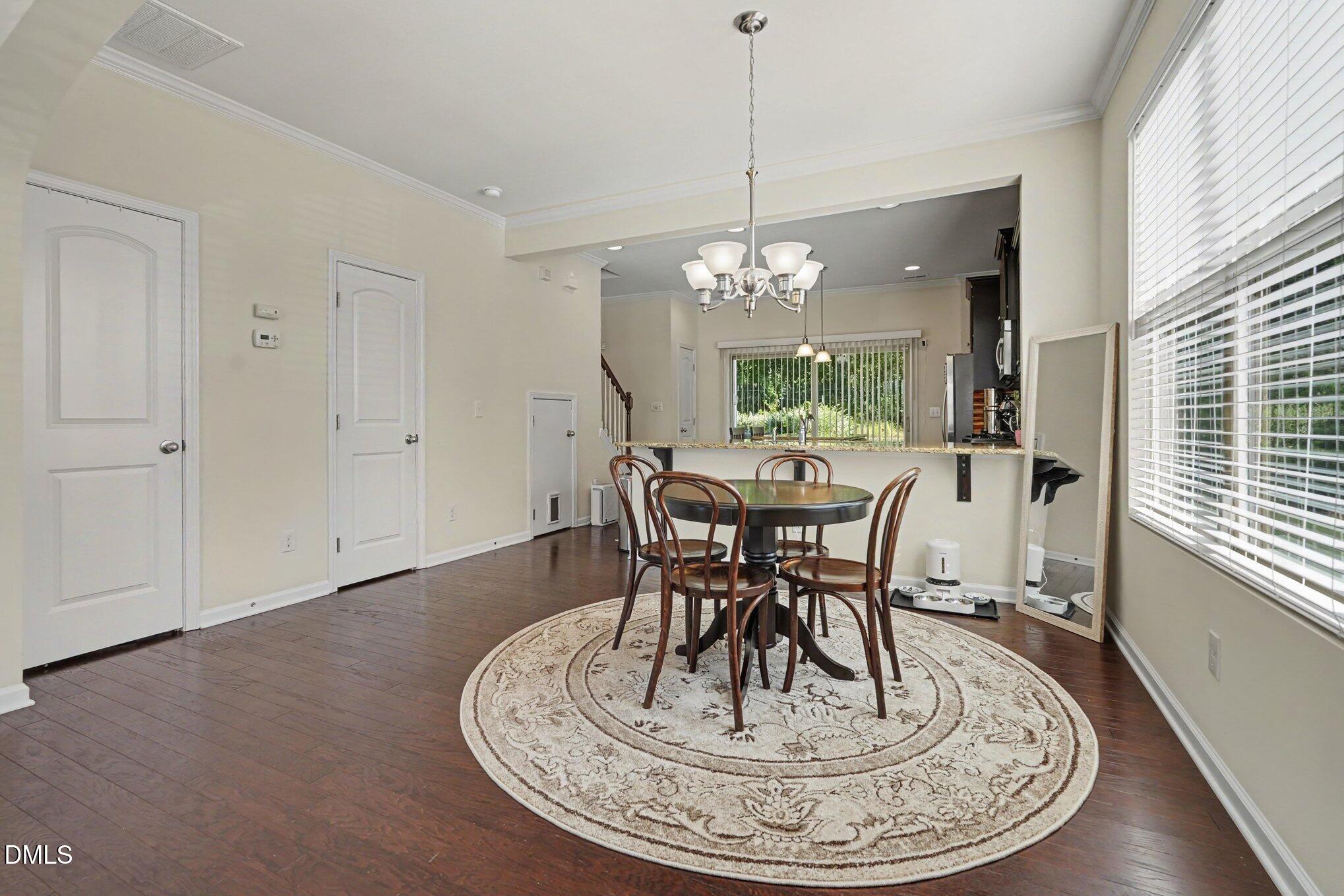 Dining area with a round table on a patterned rug, opening to a kitchen breakfast bar.