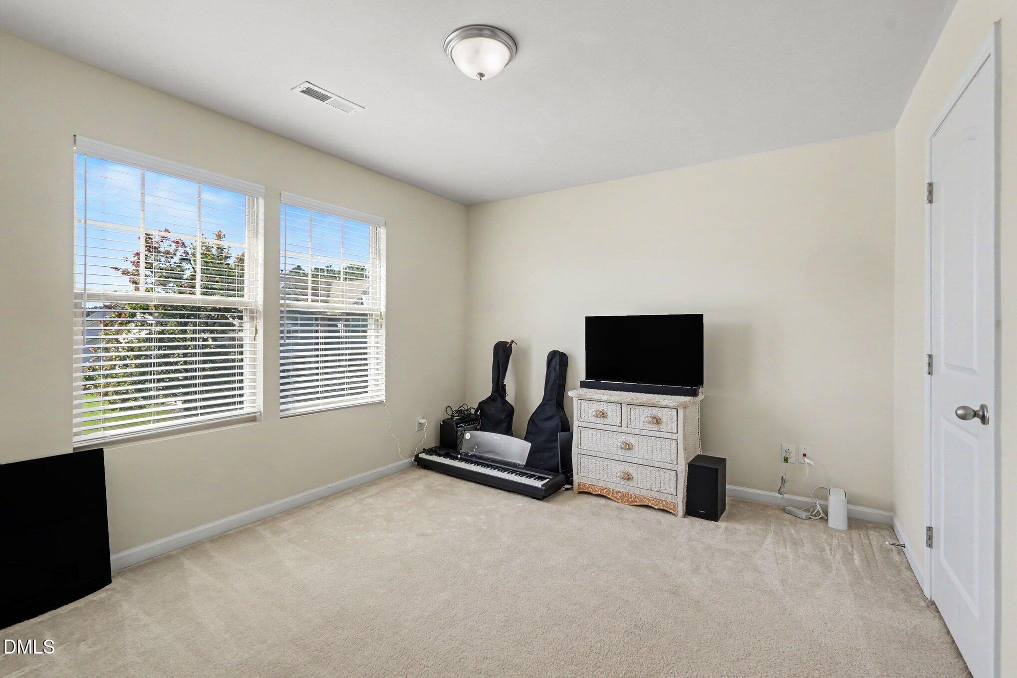 Carpeted room with two blinded windows, a digital piano, instrument cases, and a television.