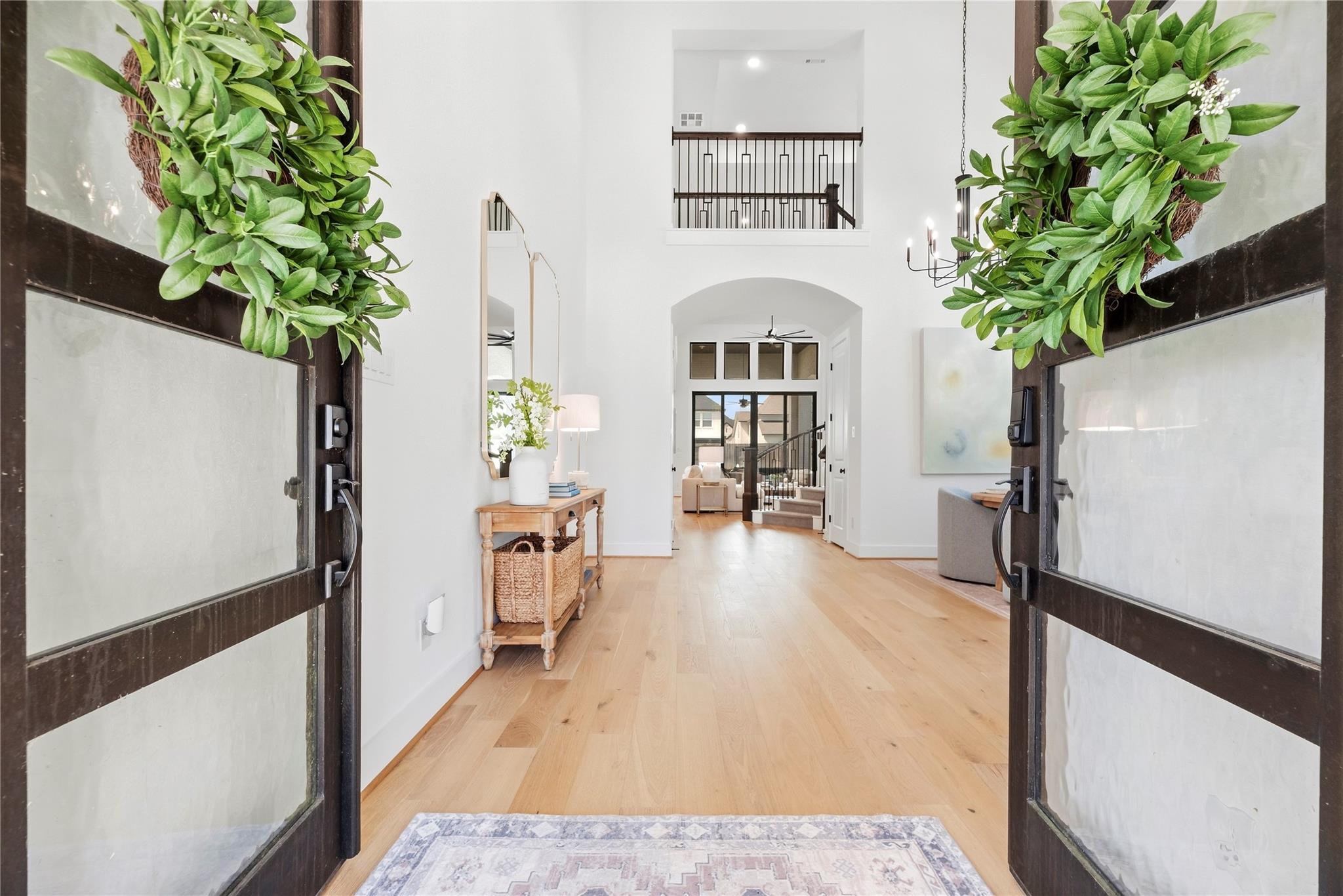 Two-story entry foyer with open glass doors, light wood floors, and a staircase beyond.