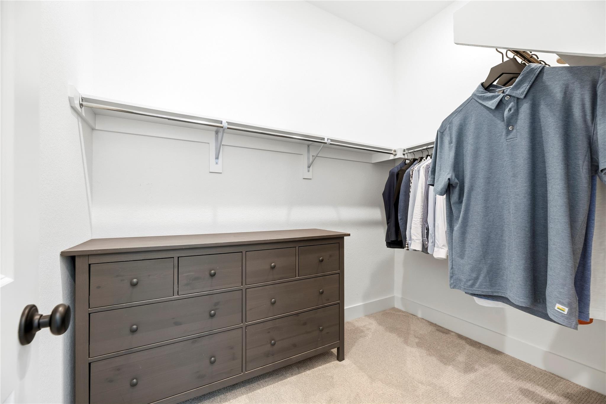 Walk-in closet with clothes on hanging rods and a dark gray chest of drawers.