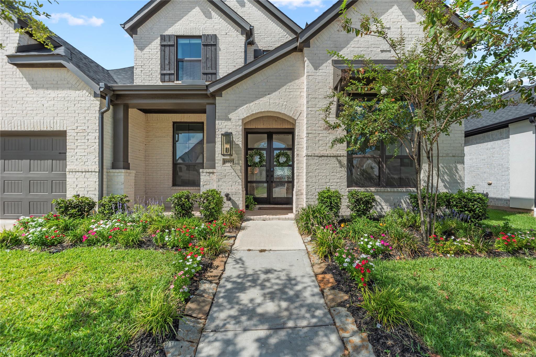 Two-story brick home with a covered entry and flower-lined walkway.