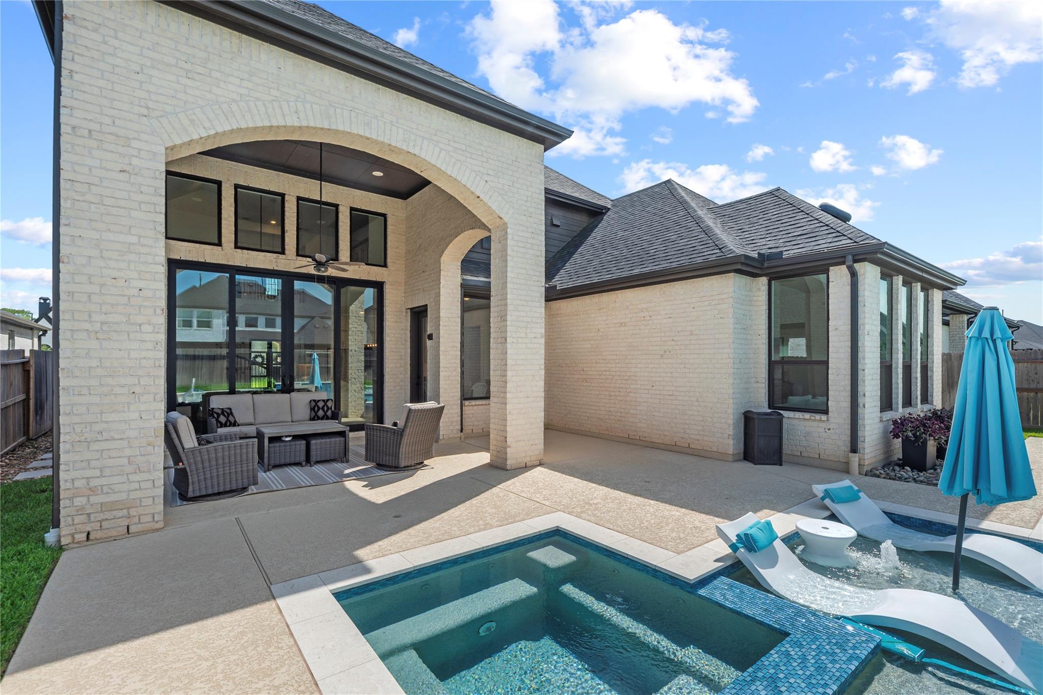 Light brick home with a covered patio overlooking a pool and shallow tanning ledge.