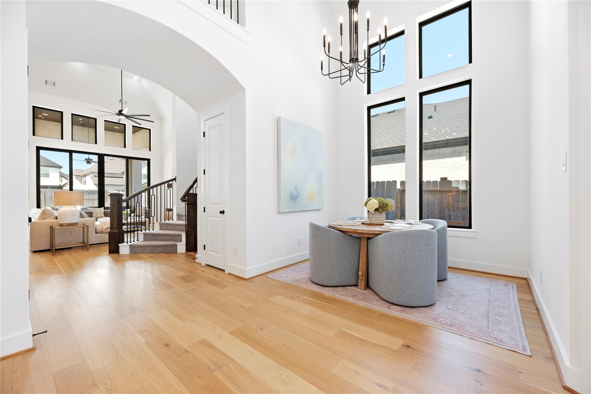 Open dining and living area with tall windows, light wood floors, and a staircase.