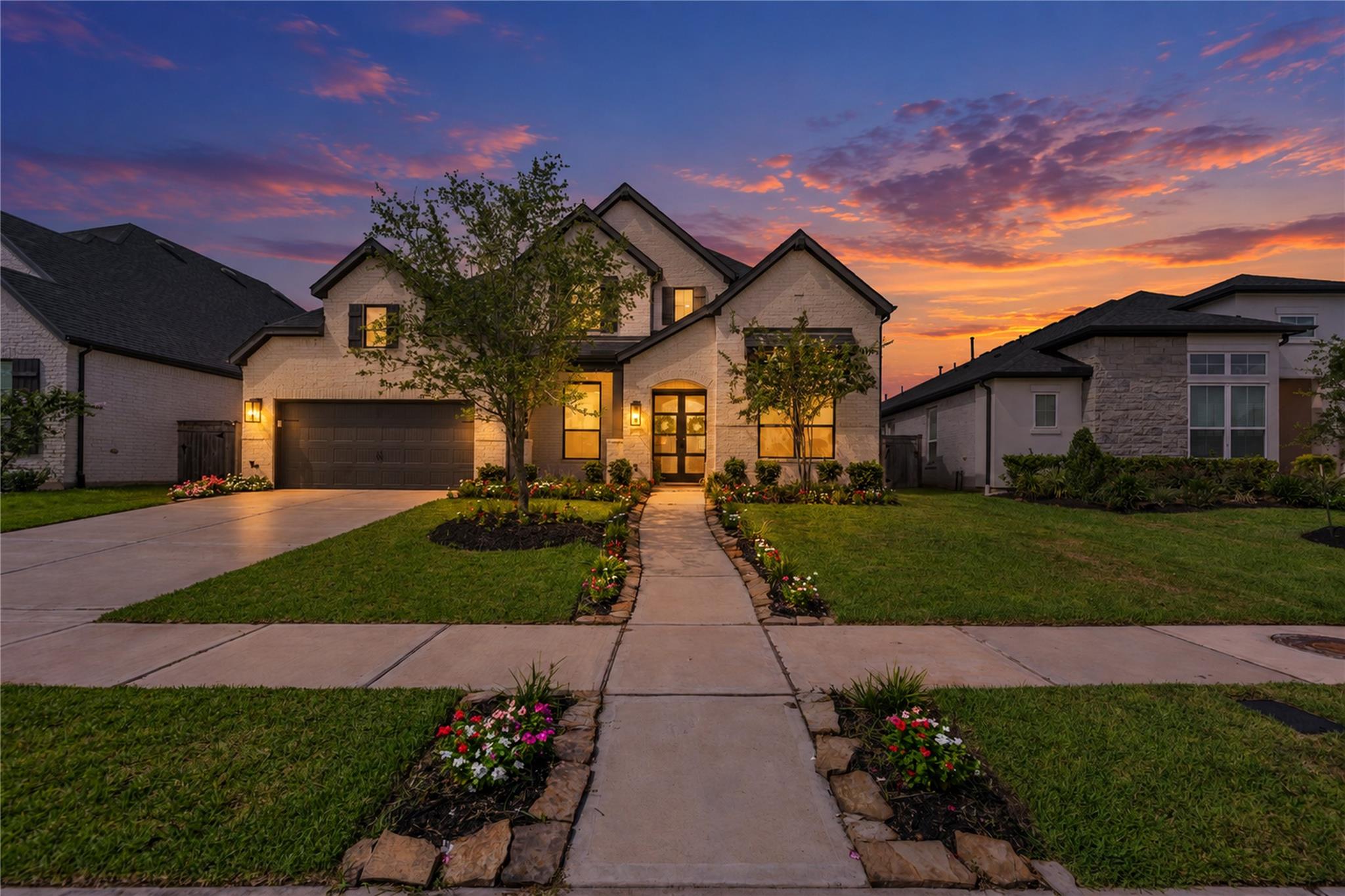 Two-story brick home with a double garage and flower-lined walkway at dusk.