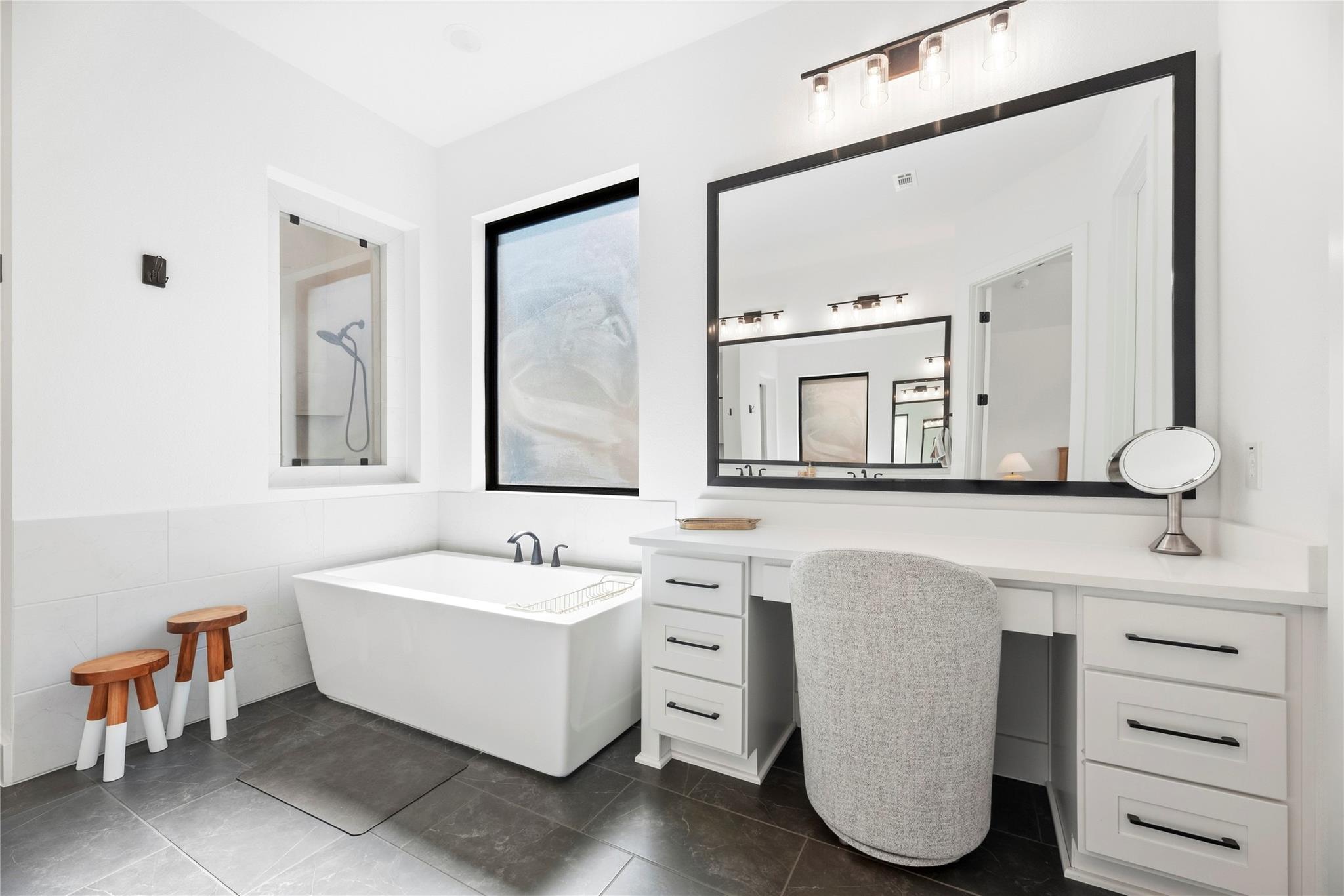 Modern bathroom with a freestanding tub beside a long white vanity and black-framed mirror.