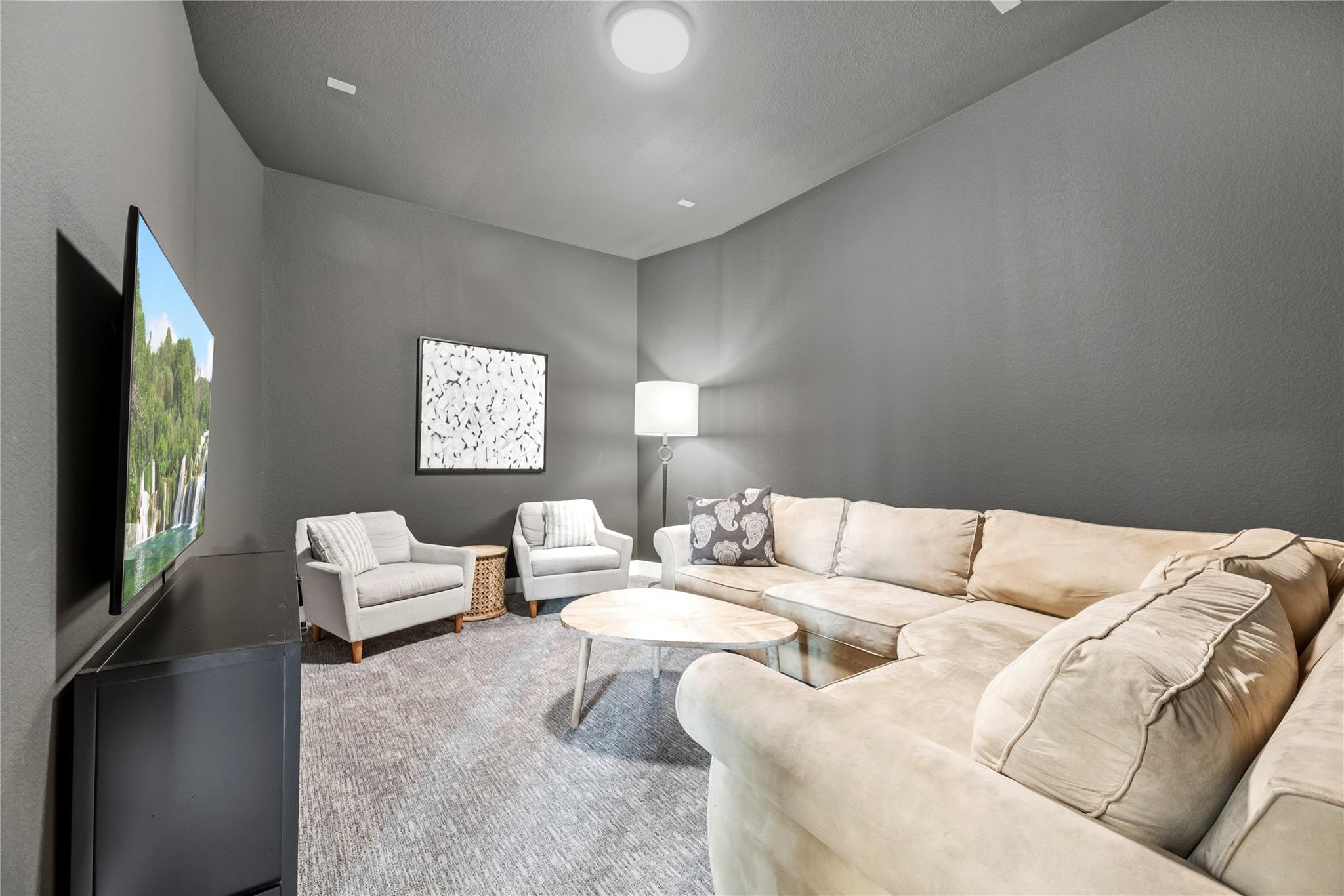 Media room with a cream sectional, two armchairs, and a large television against charcoal walls.