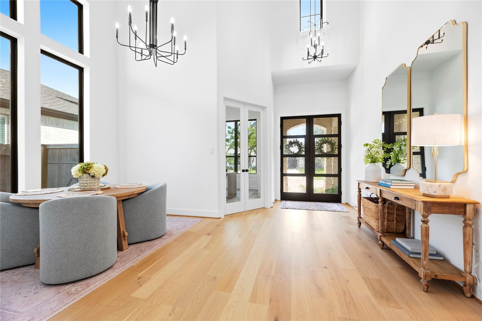 Bright entryway with black glass-paneled front doors, tall windows, and an adjoining dining area.