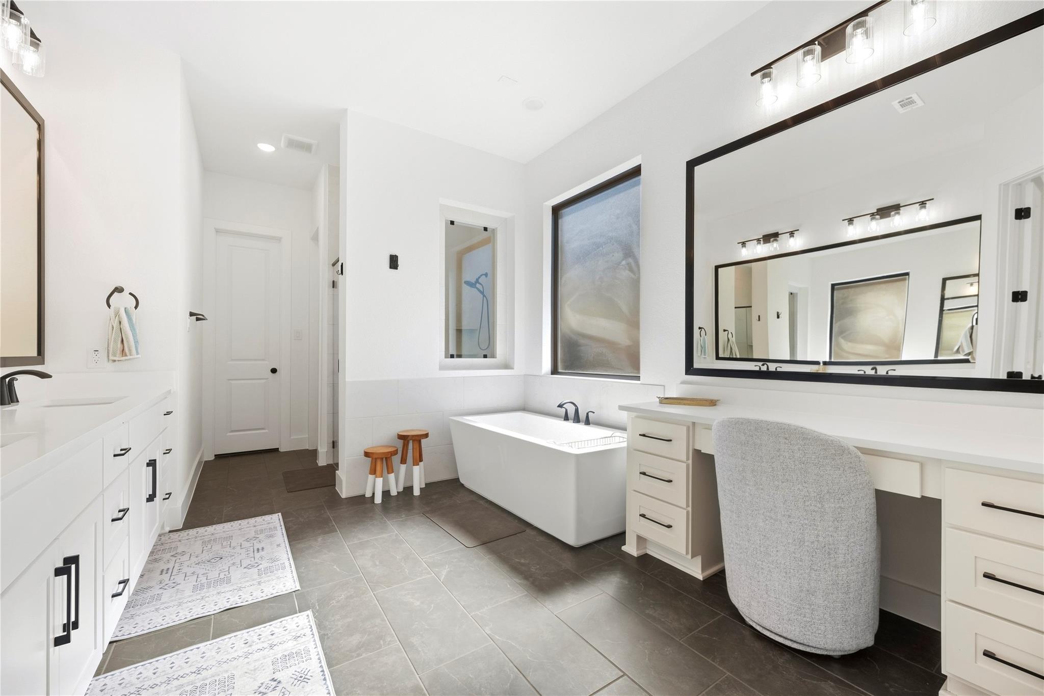 Bright primary bathroom with a freestanding tub, long double vanity, and large black-framed mirror.