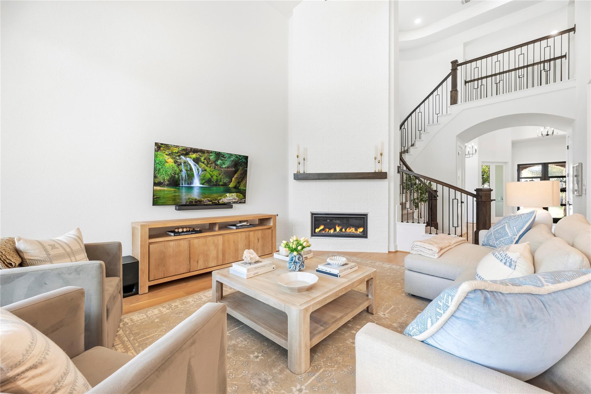 Living room with a white brick fireplace, mounted TV, and curved staircase with dark railings.