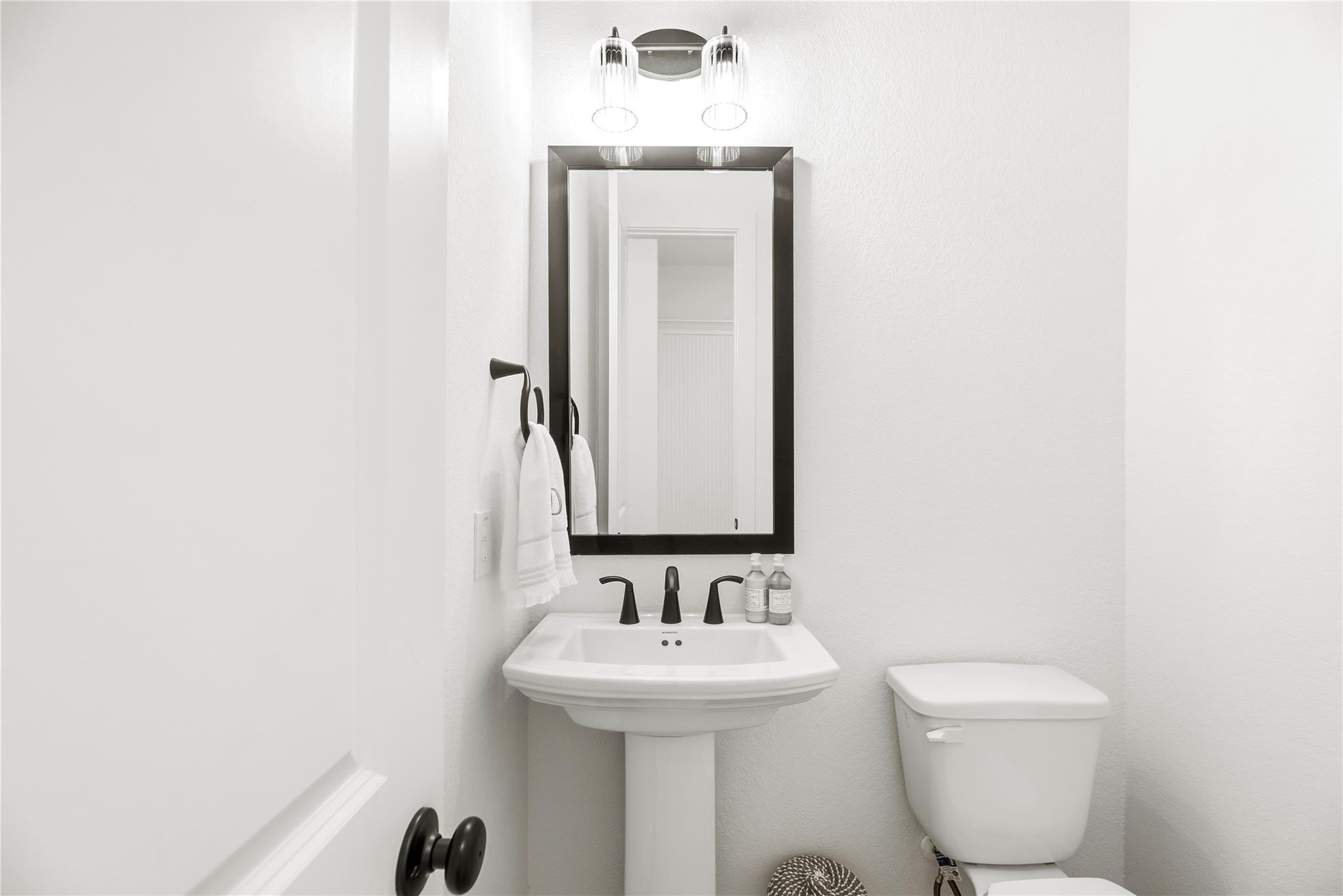 Bathroom with a white pedestal sink, black-framed mirror, and toilet.