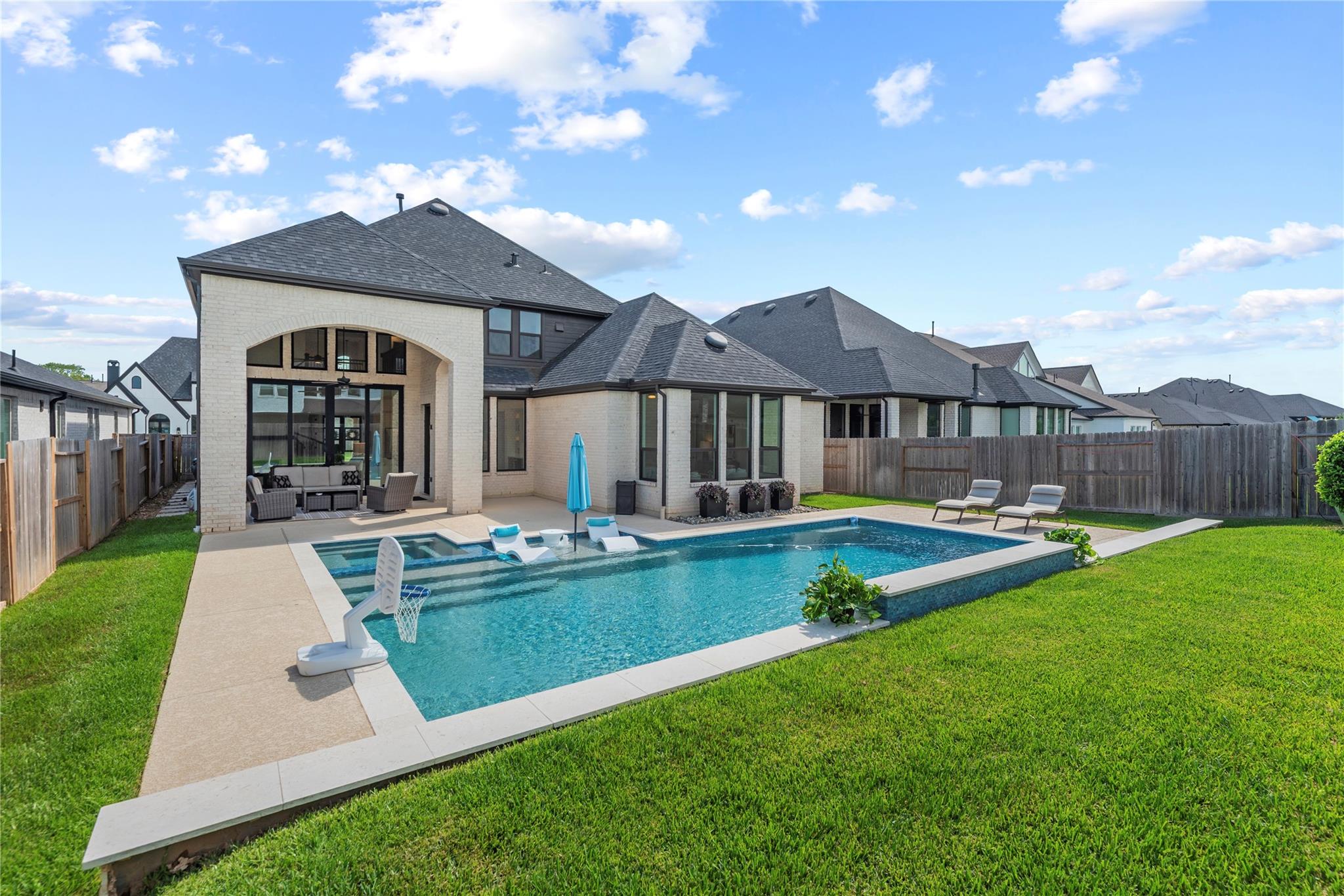 Backyard pool with tanning ledges and loungers beside a light brick house and covered patio.
