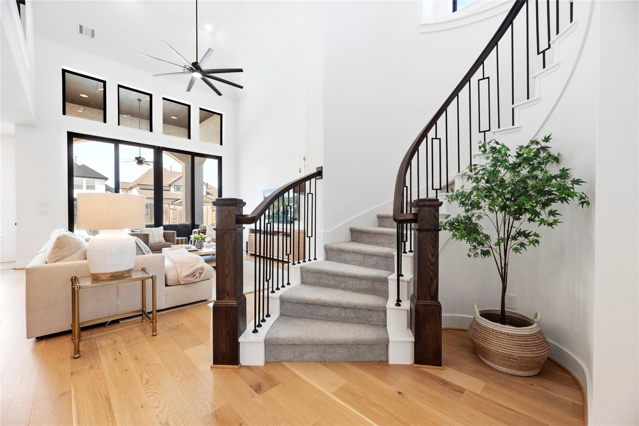 Two-story foyer with a curved staircase, black metal railings, hardwood floors, and a bright sitting area.