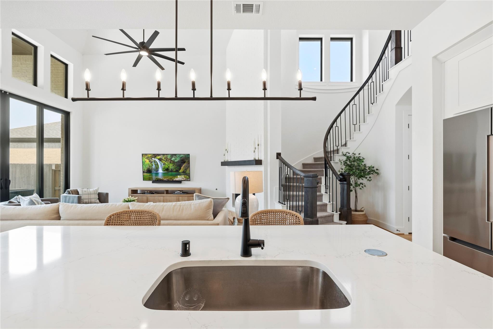Open-plan kitchen and living room with a white island, tall windows, and a curved staircase.