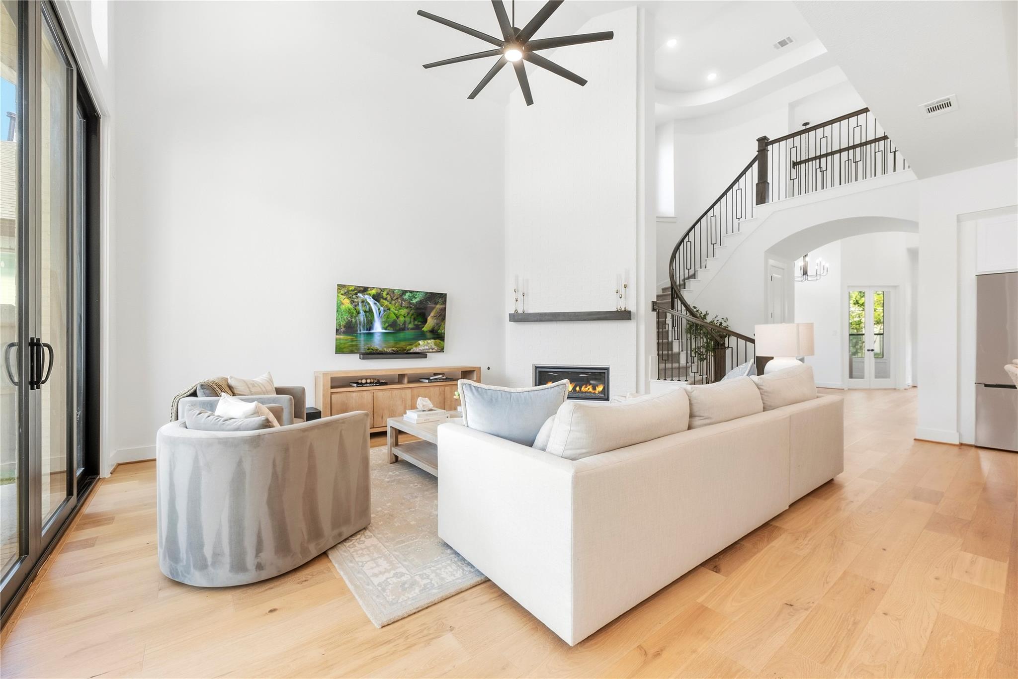 Furnished living room with a curved staircase, fireplace, and tall sliding glass doors.