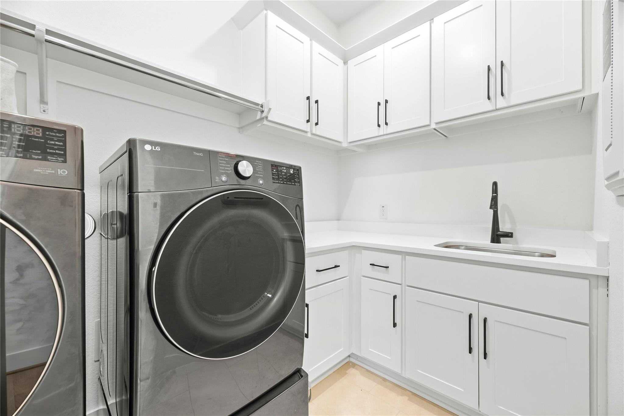 Laundry room with white cabinetry, utility sink, and dark gray front-loading washer and dryer.