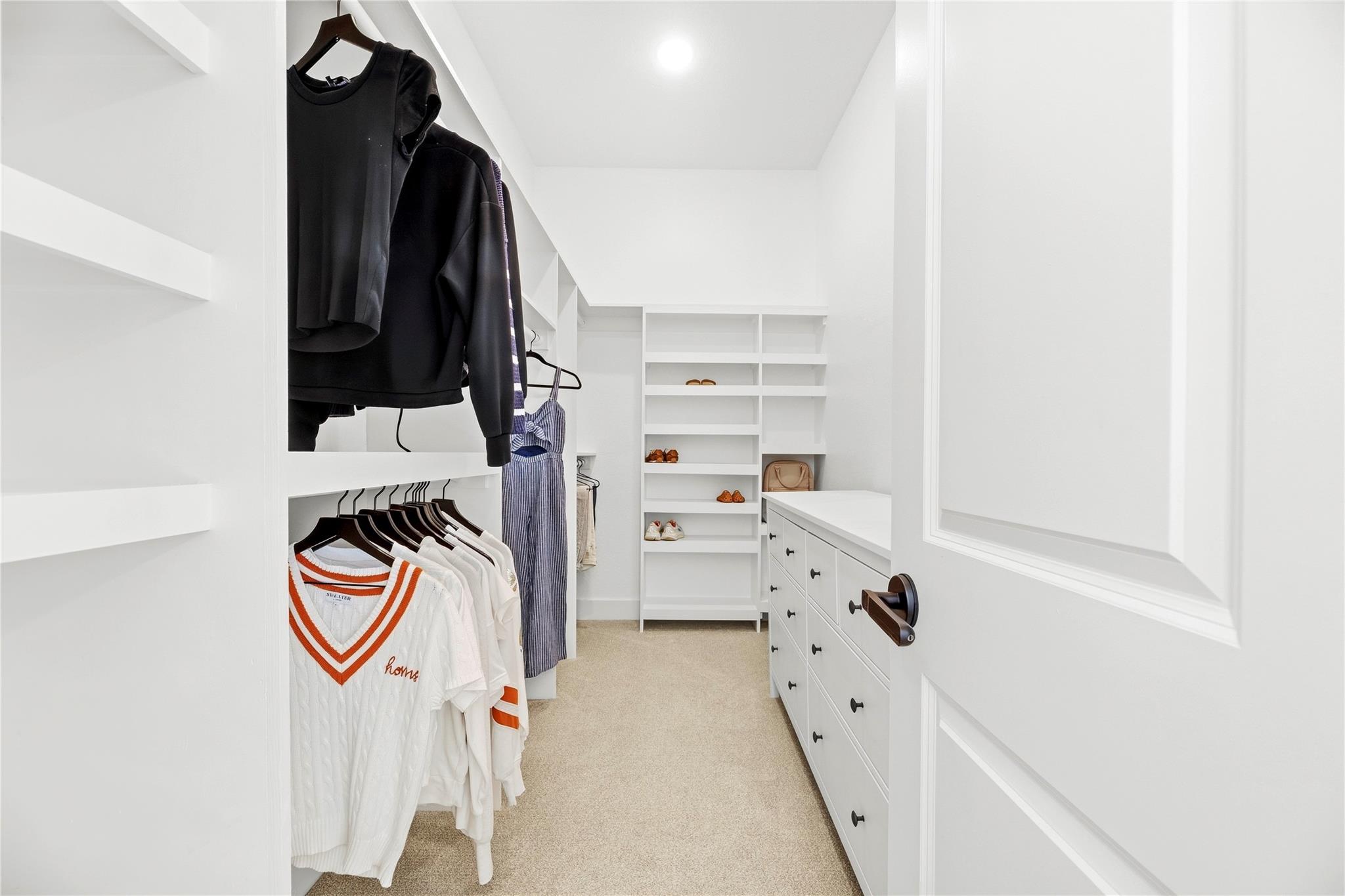Walk-in closet with built-in shelves and drawers, hanging clothes, and beige carpet.