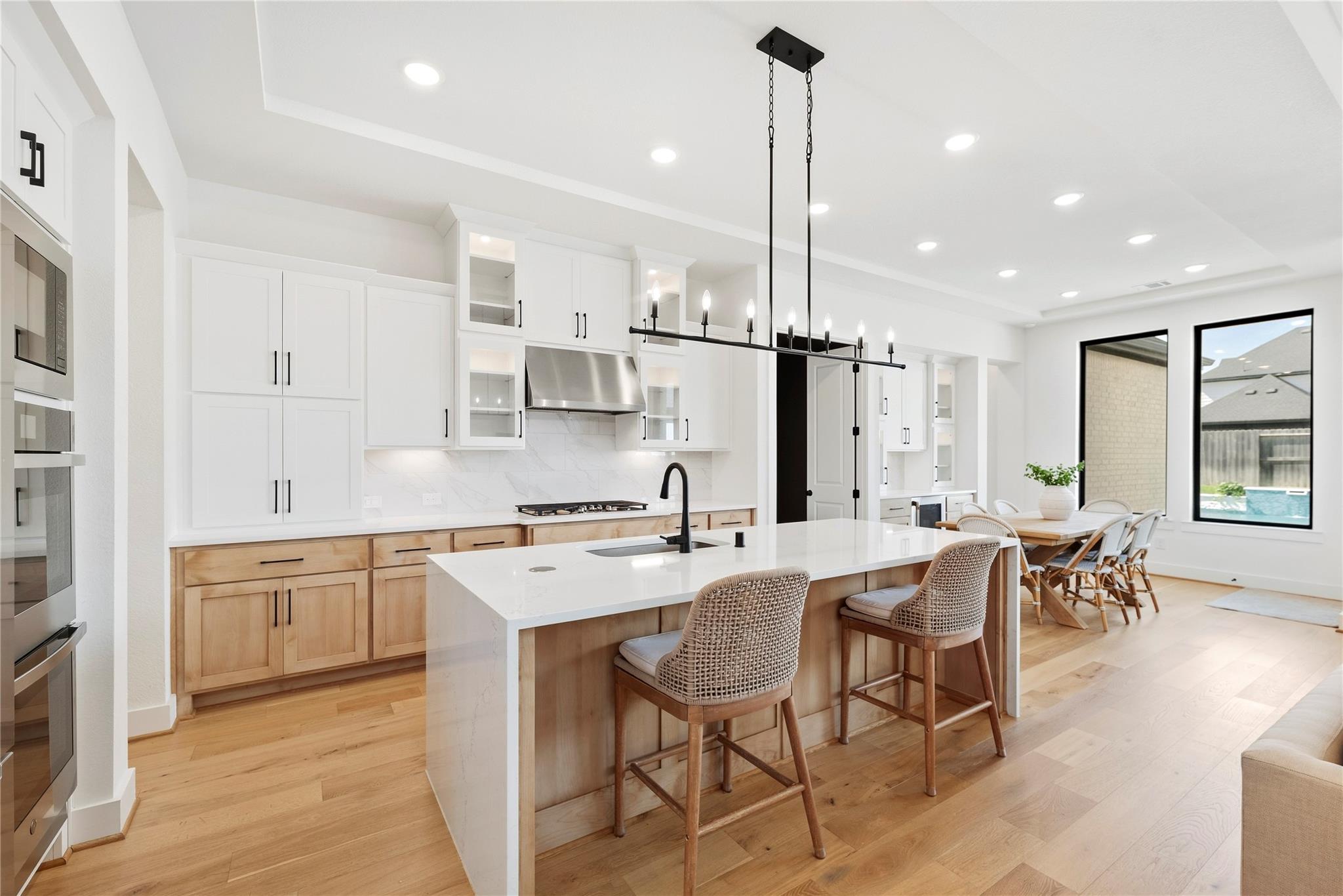Bright kitchen with white cabinetry, wood lower cabinets, a large island, and an adjoining dining area.