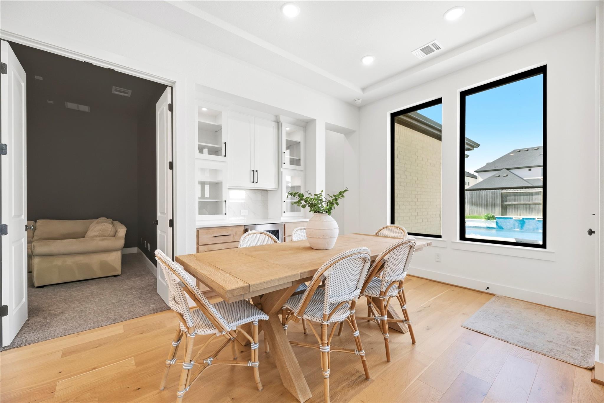 Dining room with a wood table, built-in cabinetry, and windows overlooking a backyard pool.