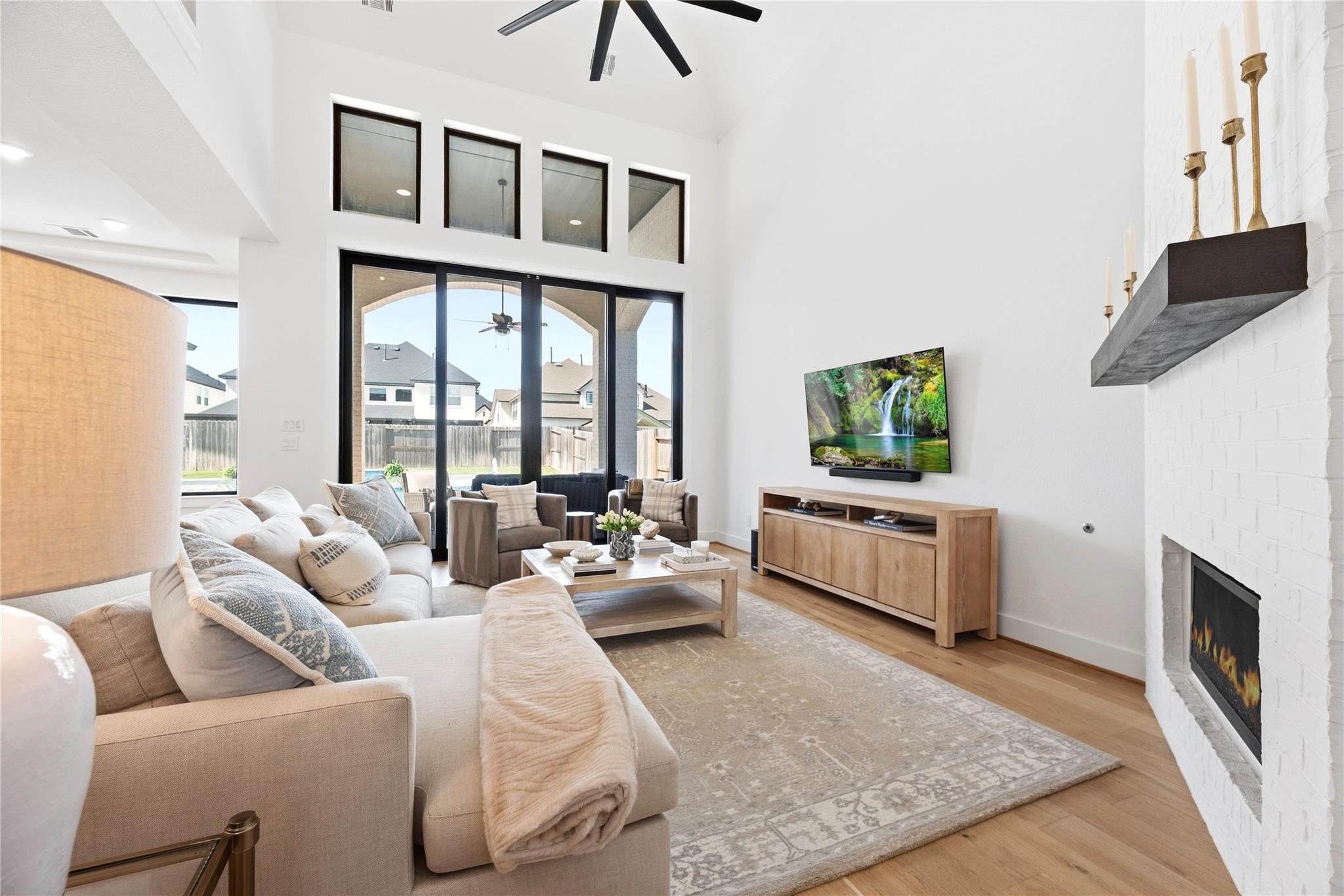 Vaulted living room with tall glass doors, neutral seating, and a white brick fireplace.