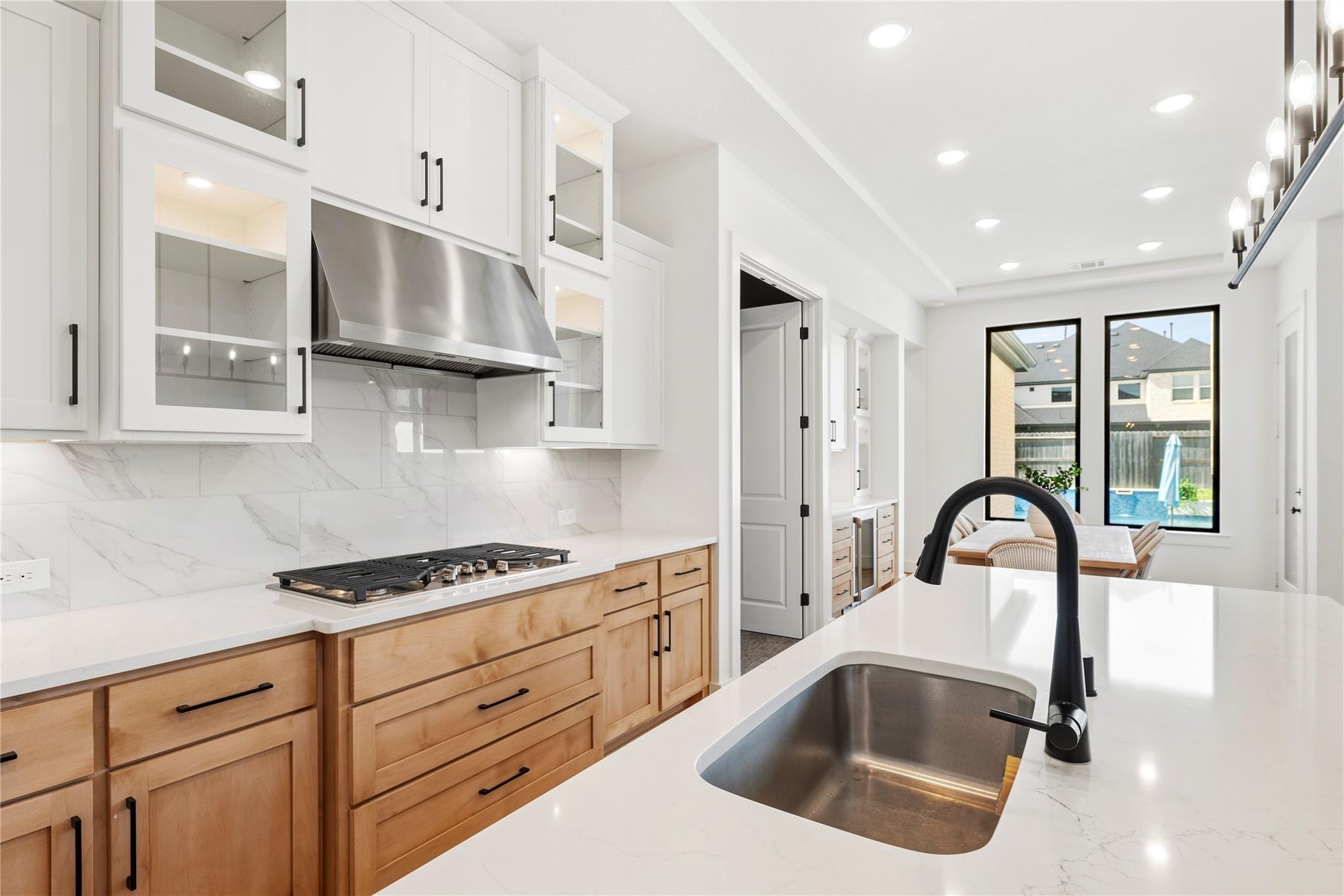 Modern kitchen with wood cabinetry, a large white island, and views of the backyard pool.