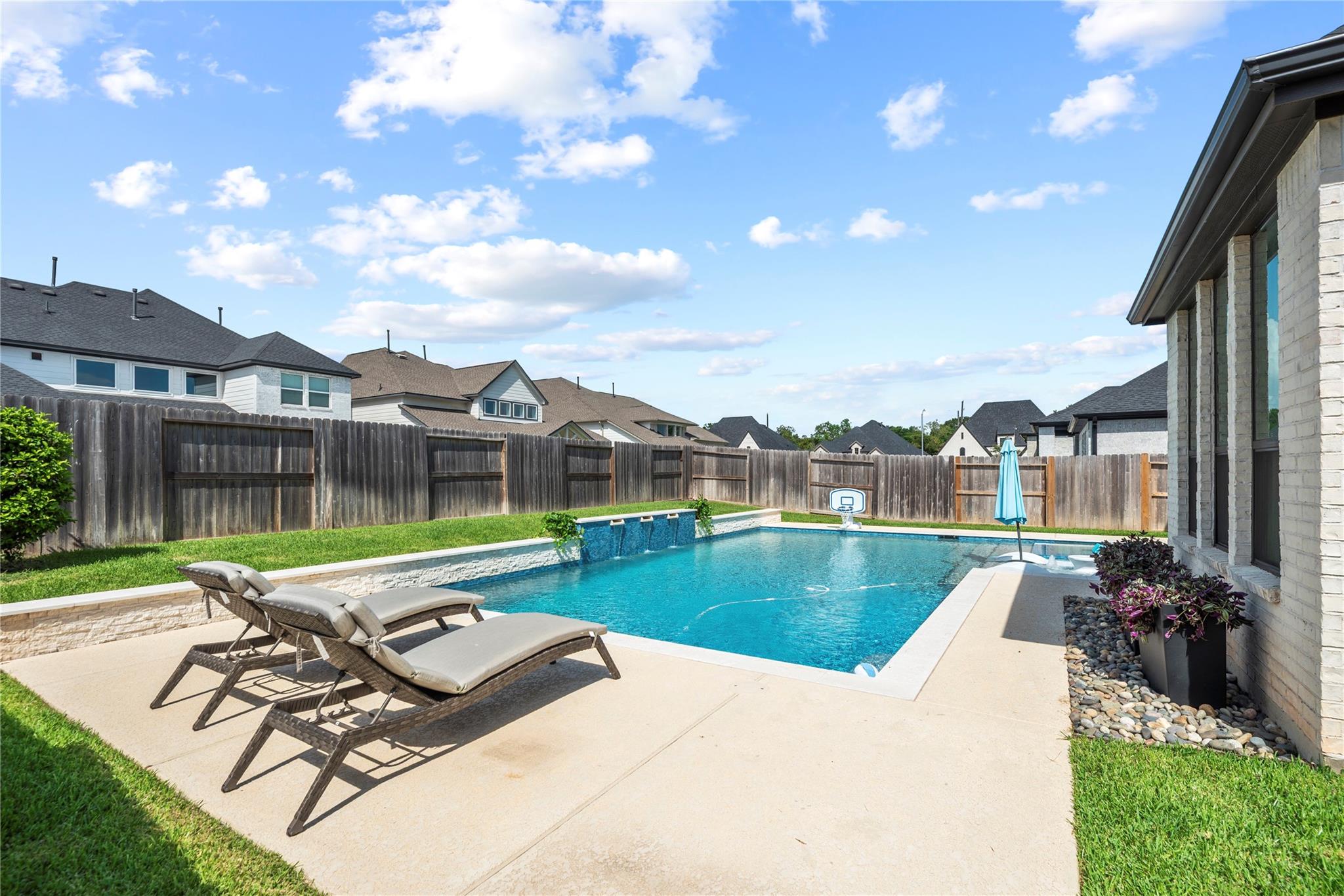 Backyard swimming pool with stone patio, chaise lounges, and a basketball hoop.