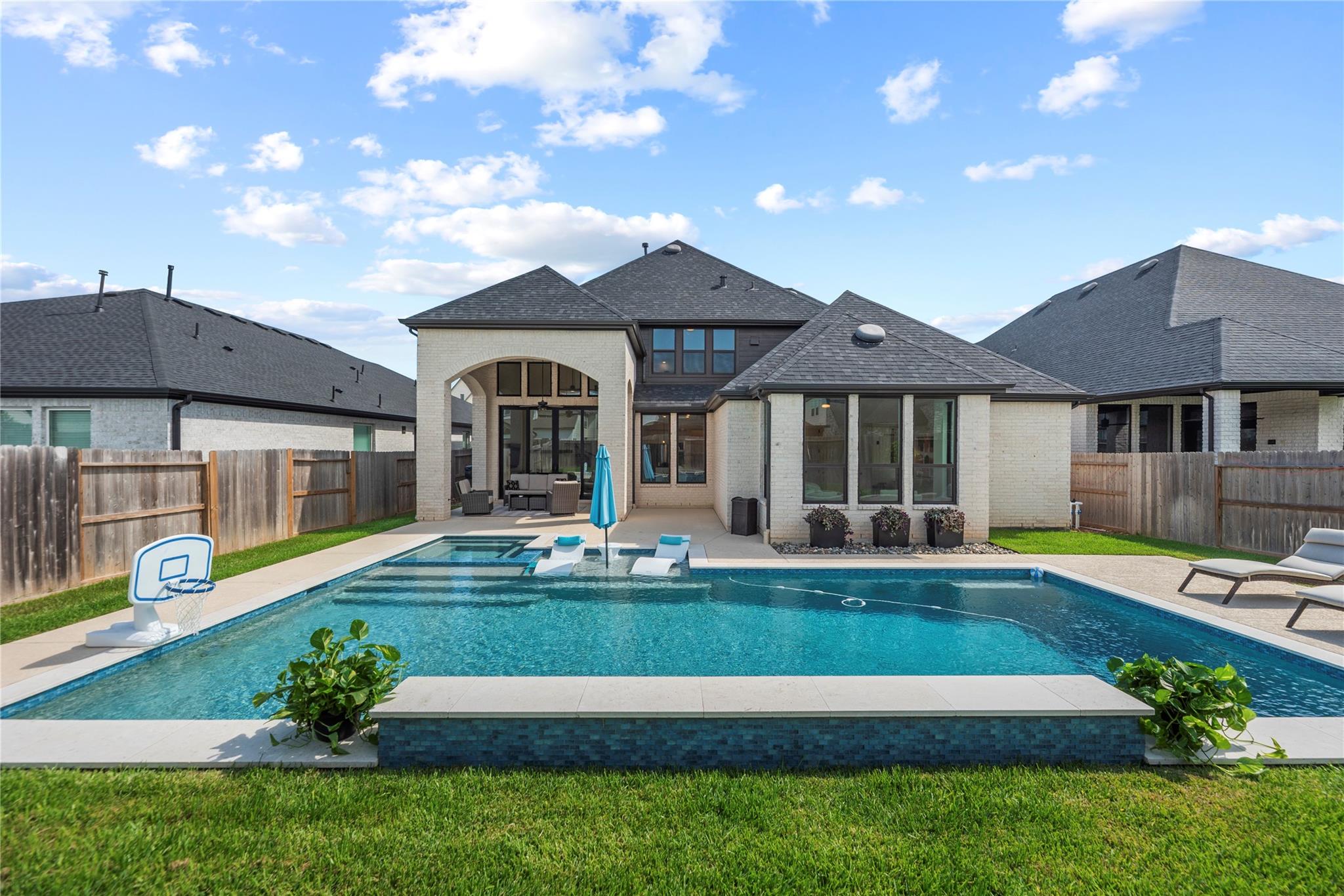 Backyard pool with raised spa and loungers beside a two-story brick home.