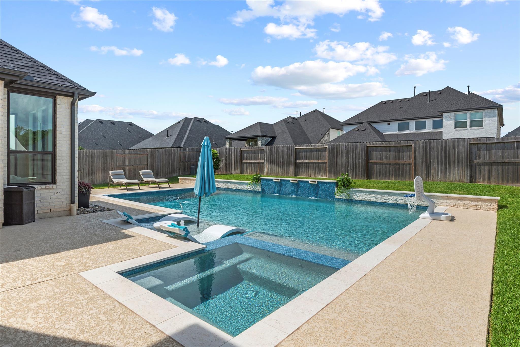 Backyard swimming pool with a shallow tanning ledge, submerged loungers, and a blue umbrella.