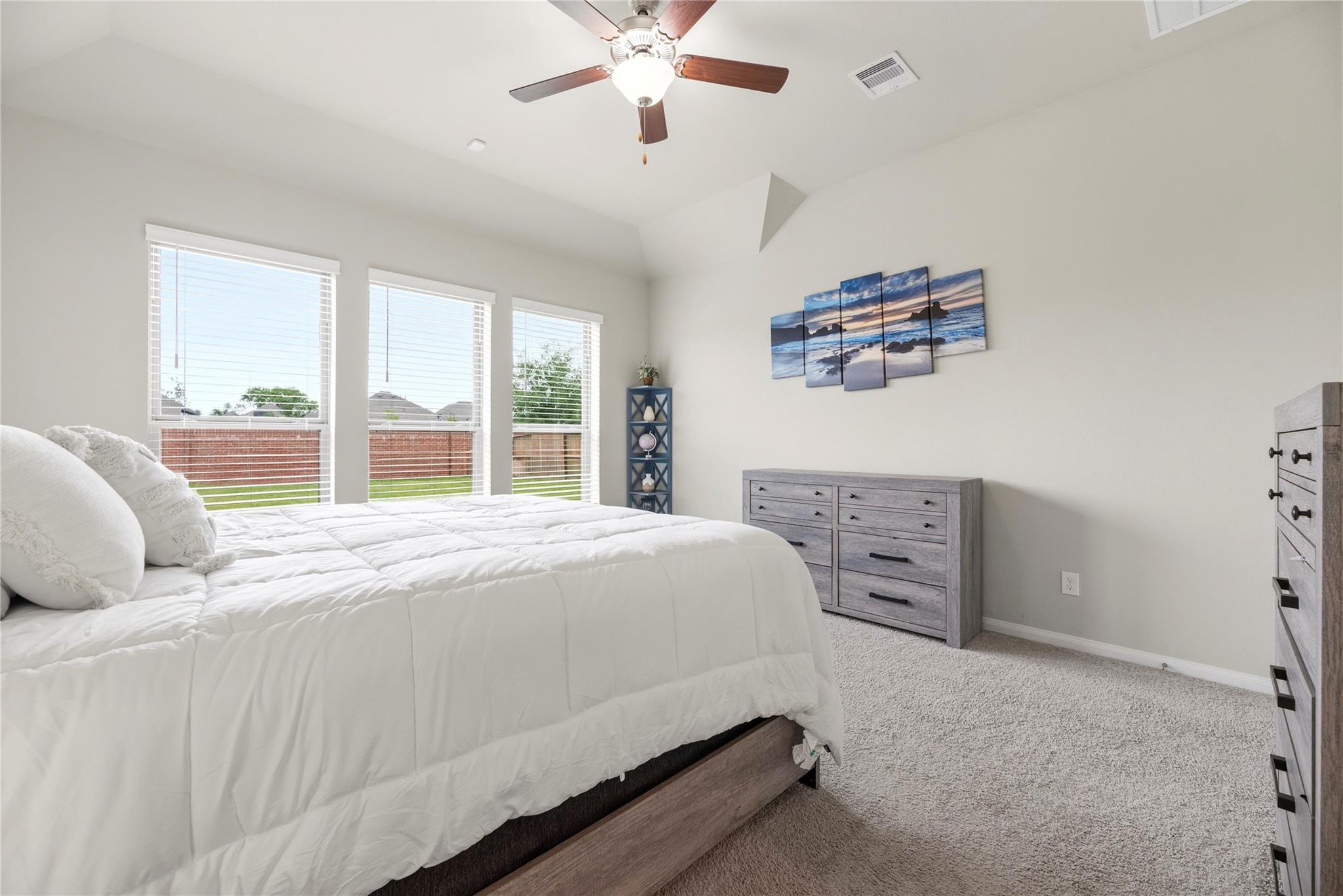 Furnished bedroom with a white bed, three windows, gray dressers, and ocean wall art.
