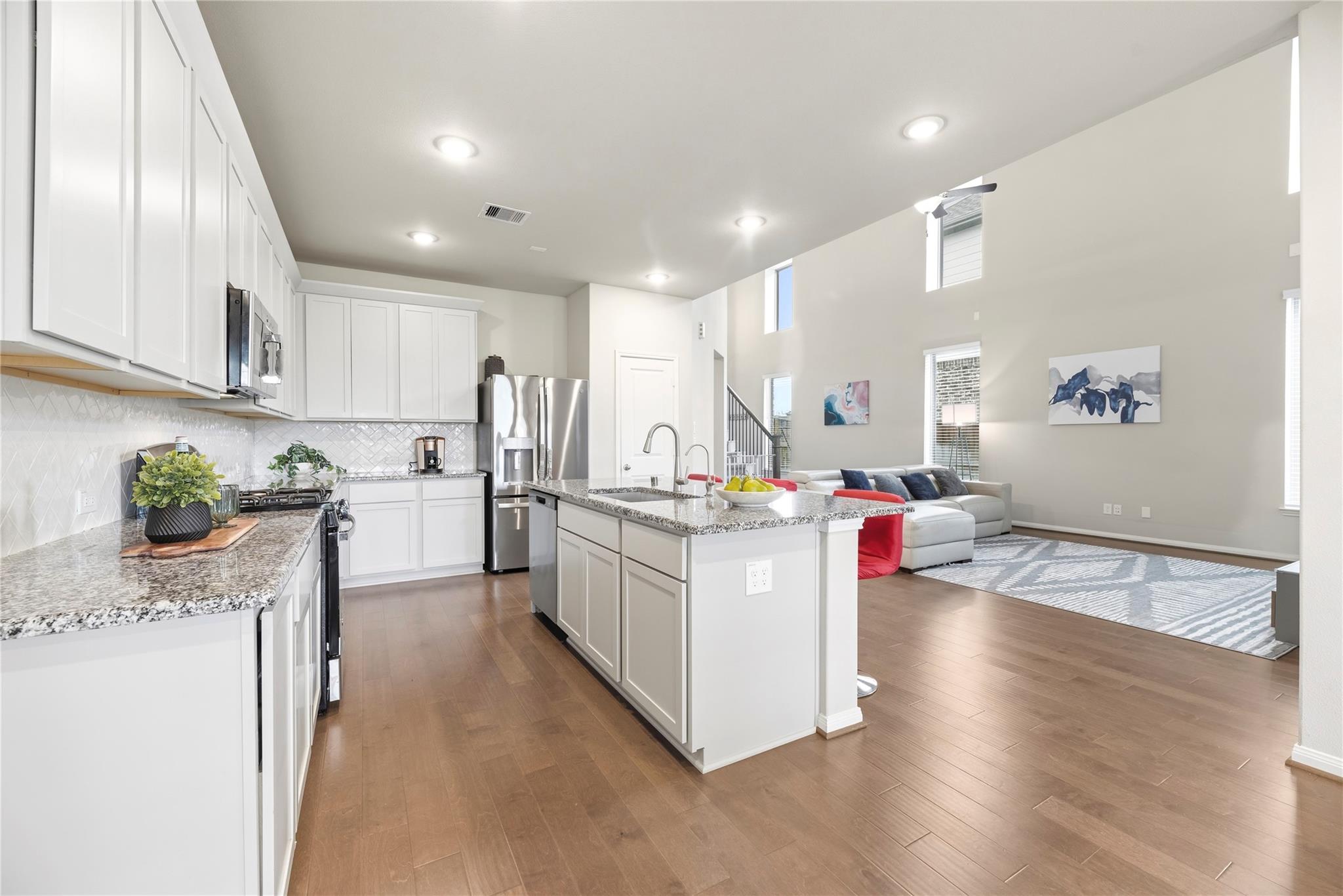 Open-plan kitchen and living room with a large granite island, white cabinets, and tall windows.