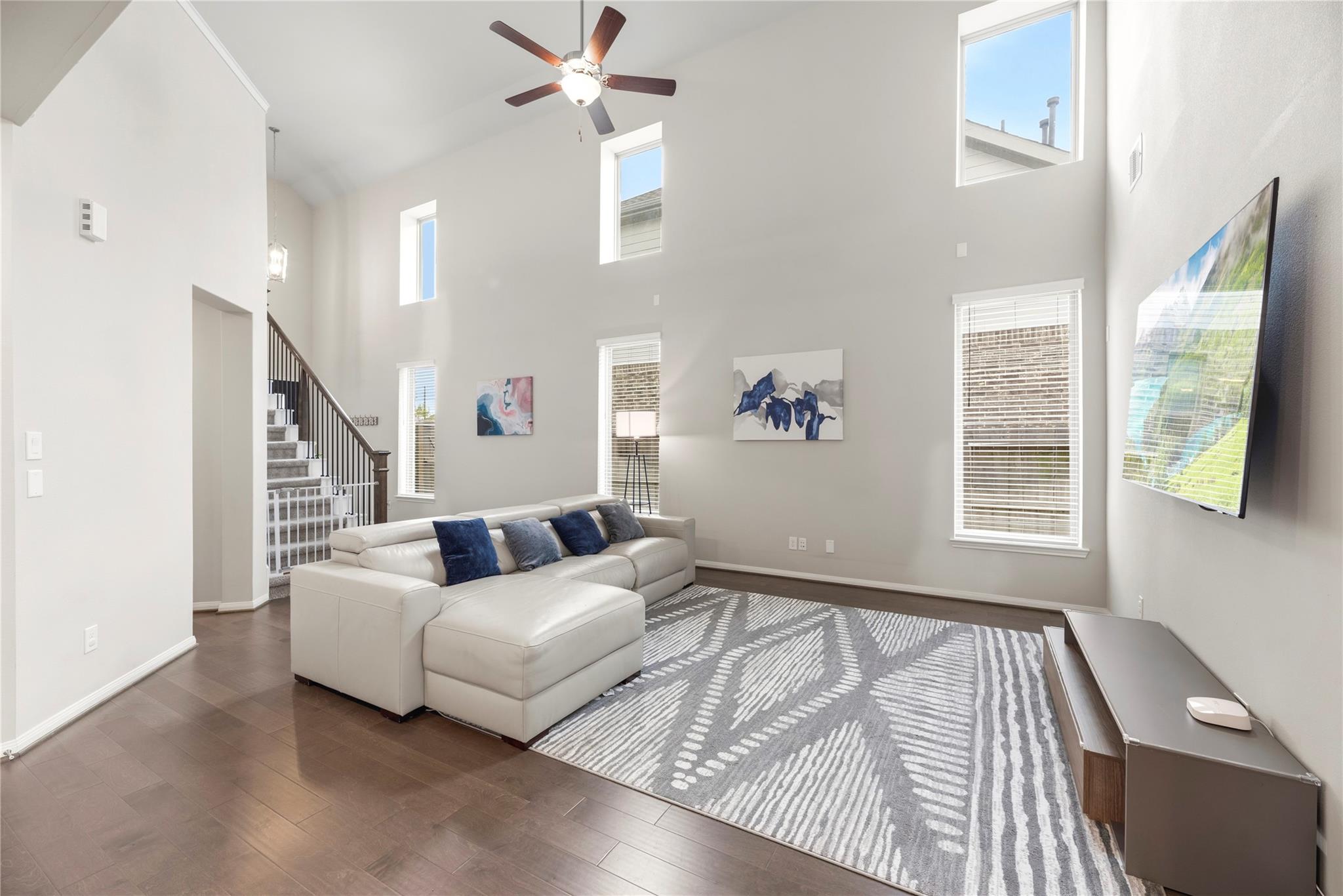 Double-height living room with a white sectional, patterned rug, tall windows, and staircase.