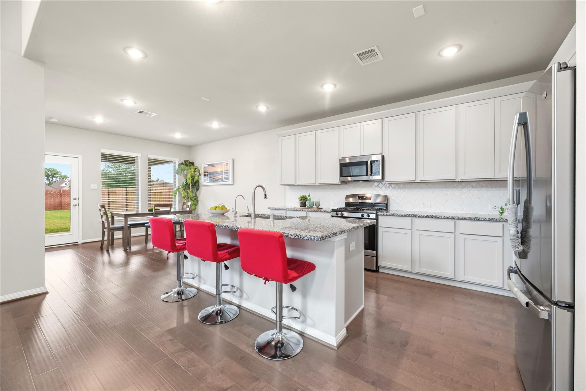 Bright kitchen with a granite island, three red stools, white cabinets, and stainless steel appliances.