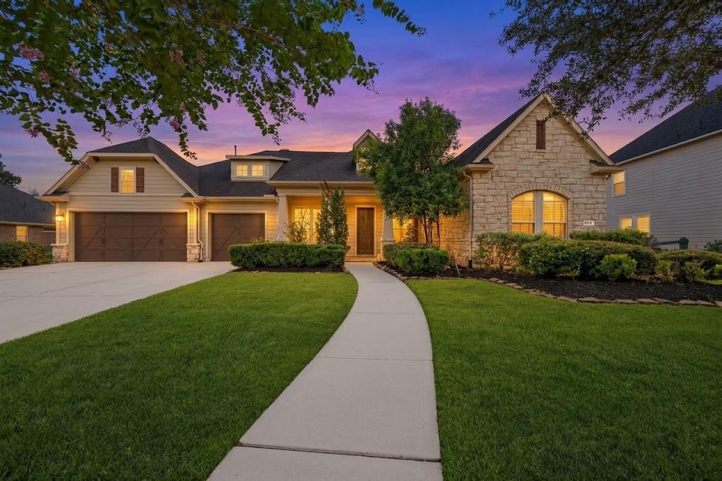 Home with a stone front, two garage doors, and a curved walkway across the lawn at dusk.