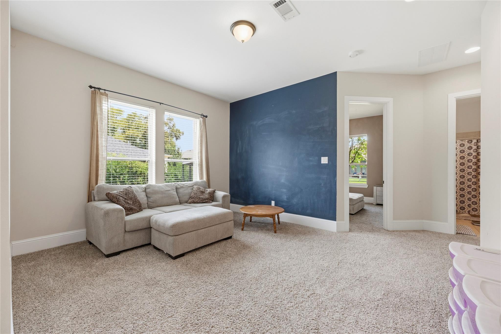 Carpeted living room with a light sectional sofa, two windows, and a dark blue accent wall.