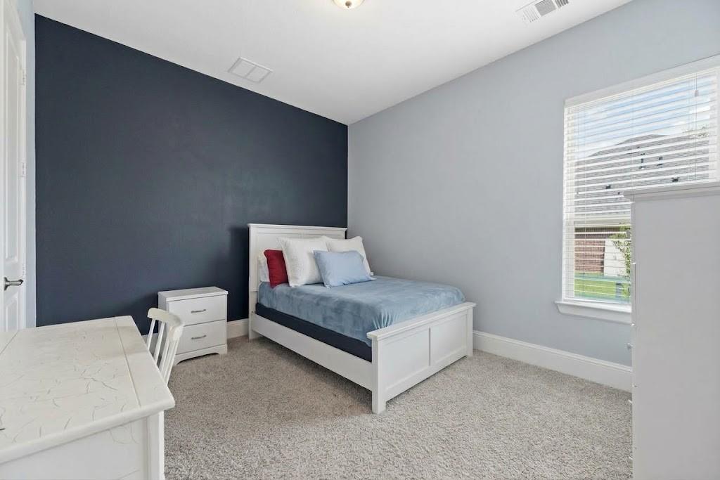 Bedroom with a white bed and pale blue bedding against a navy accent wall, beside a window with white blinds.