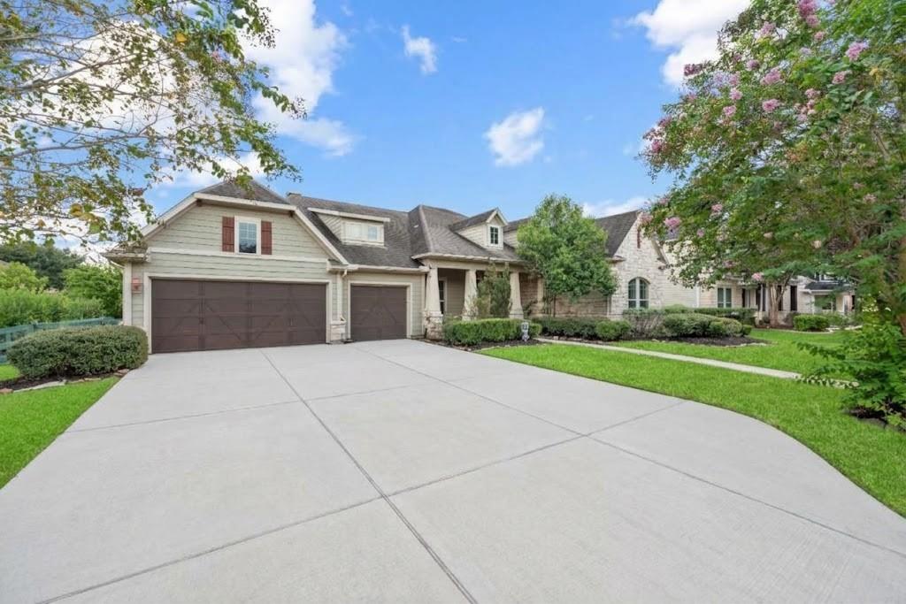 Large light-colored house with stone accents, double garage, broad driveway, and flowering trees.