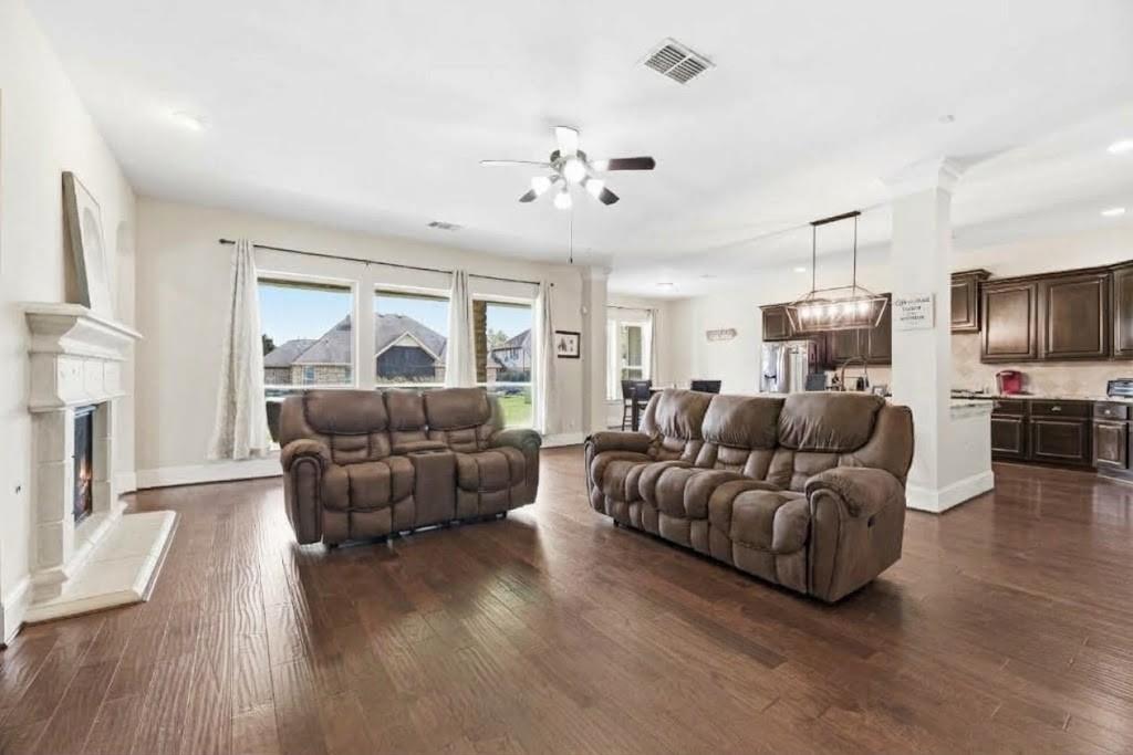 Living room with brown reclining sofas, a white fireplace, and dark hardwood floors beside the open kitchen.
